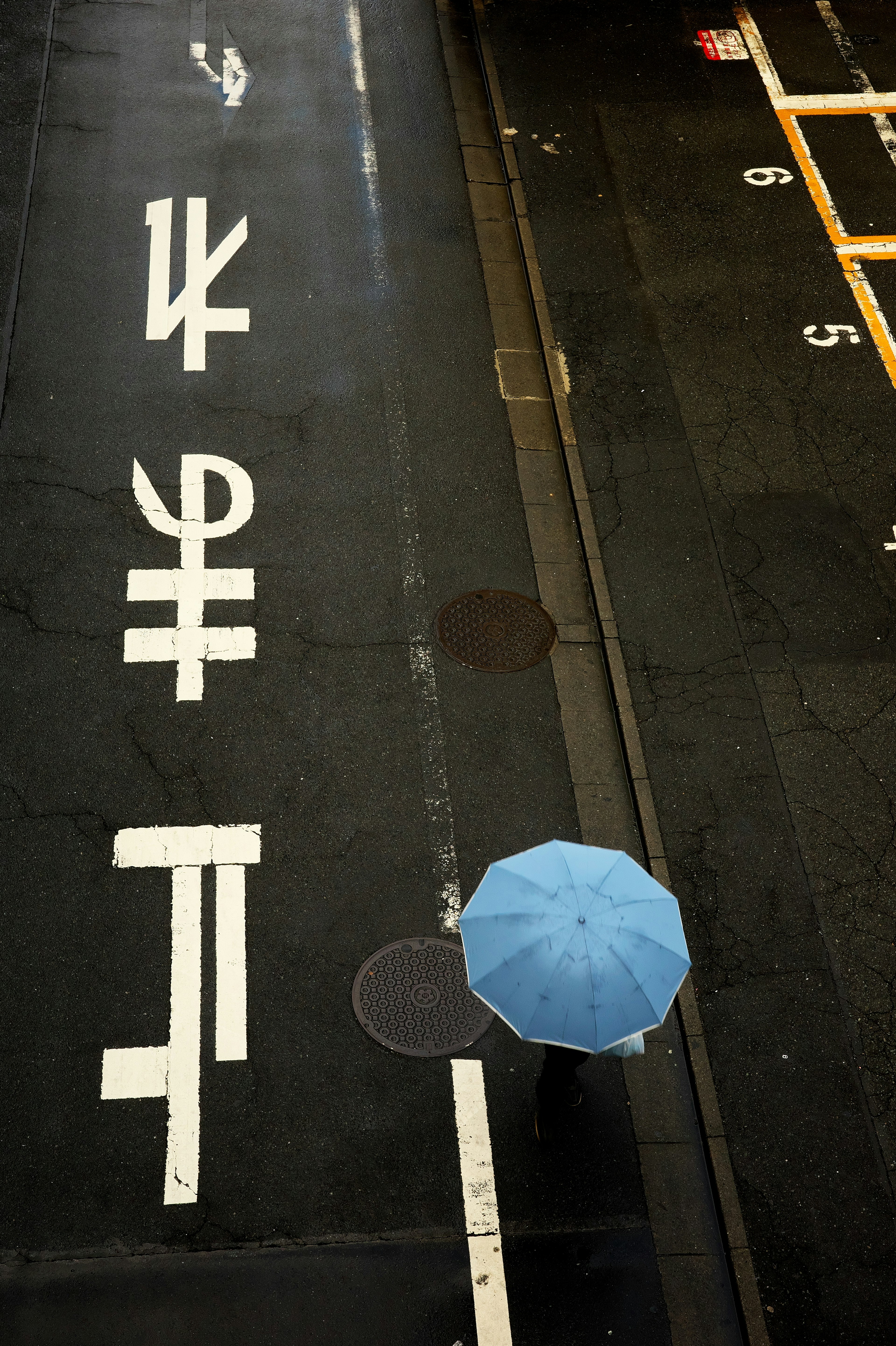 Luftaufnahme einer Straße mit einem blauen Regenschirm und weißen Markierungen