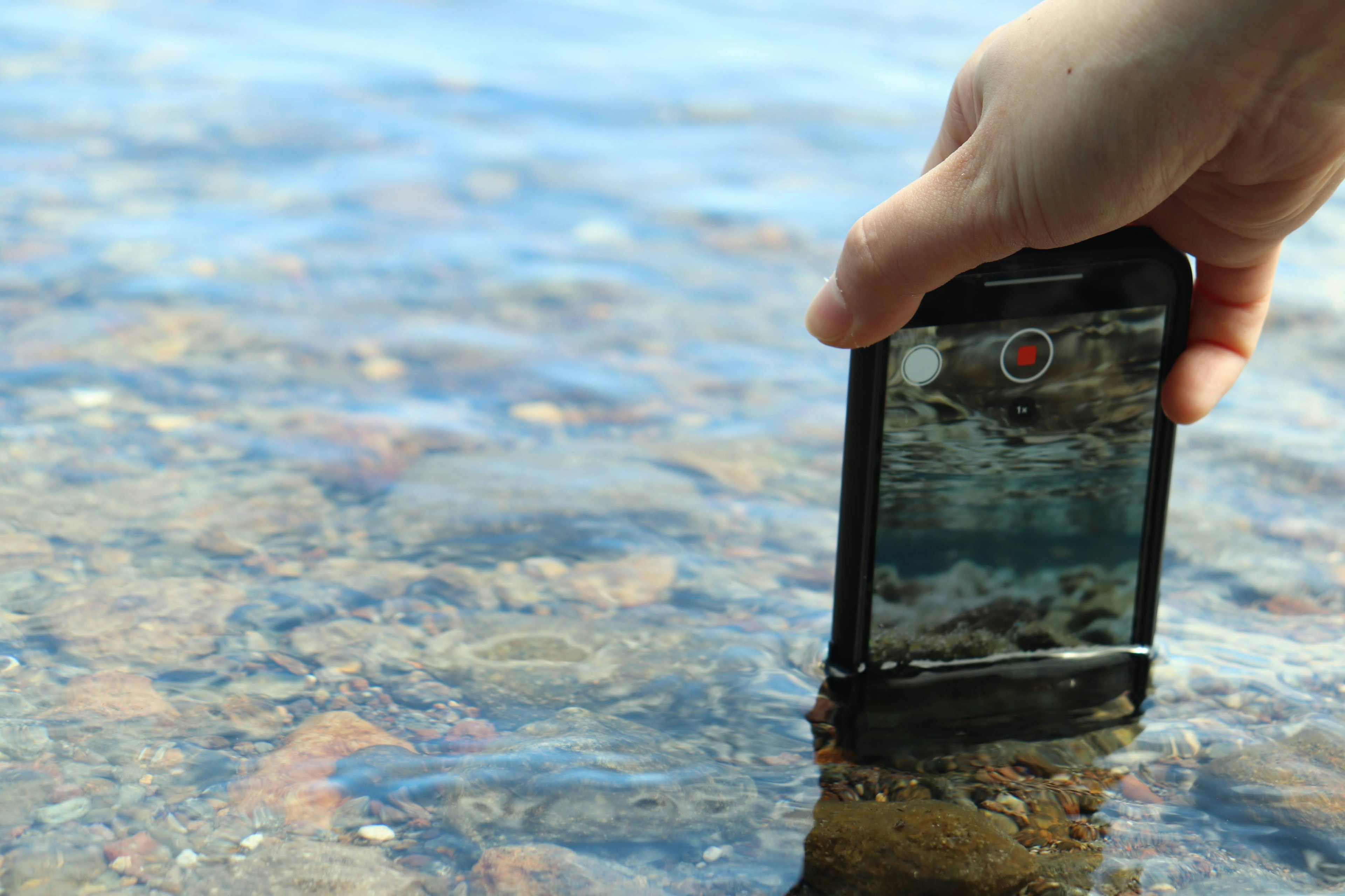 A hand holding a smartphone partially submerged in water