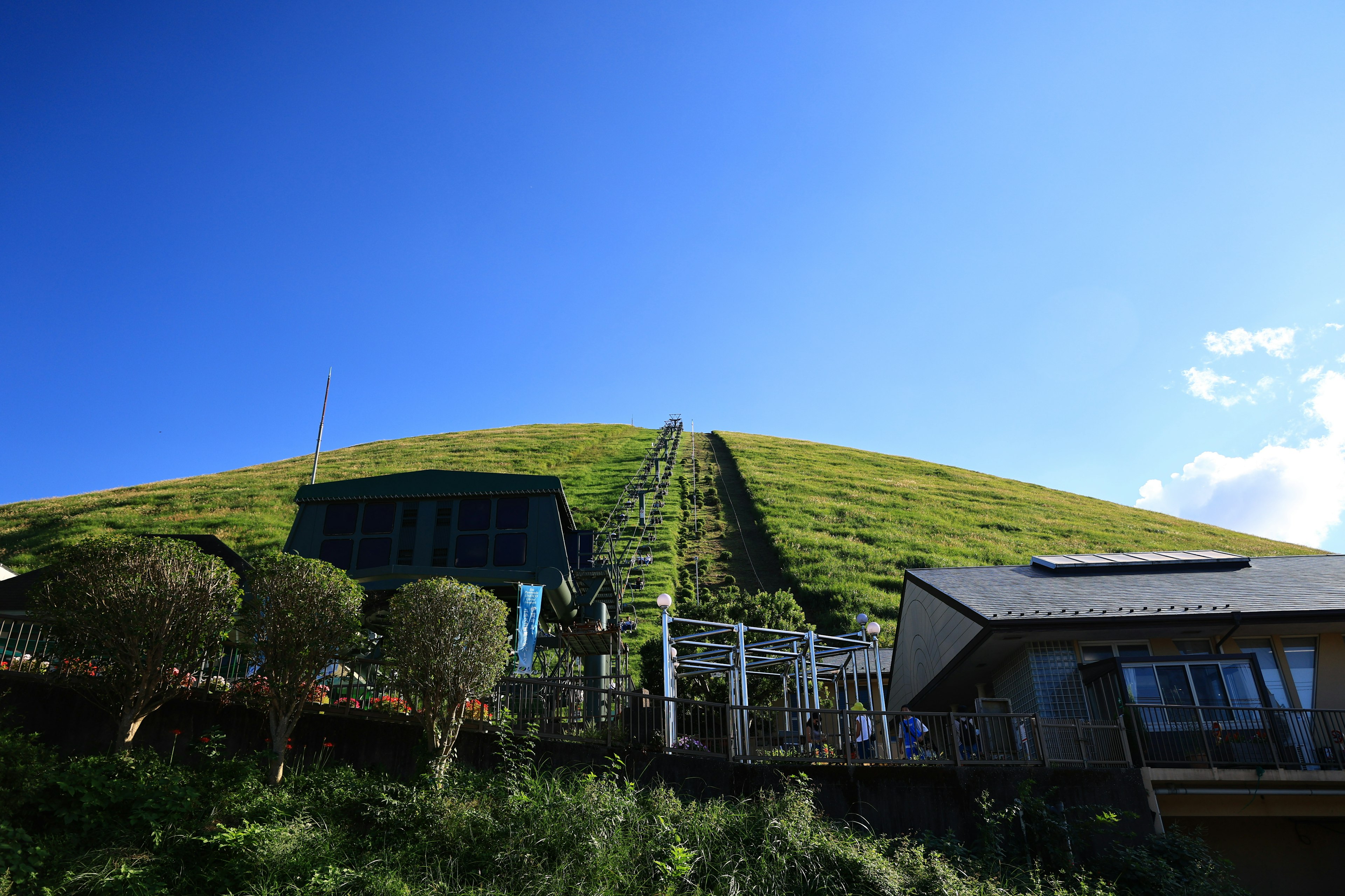 Scenic view of a green hill with a blue sky and a small building at the base