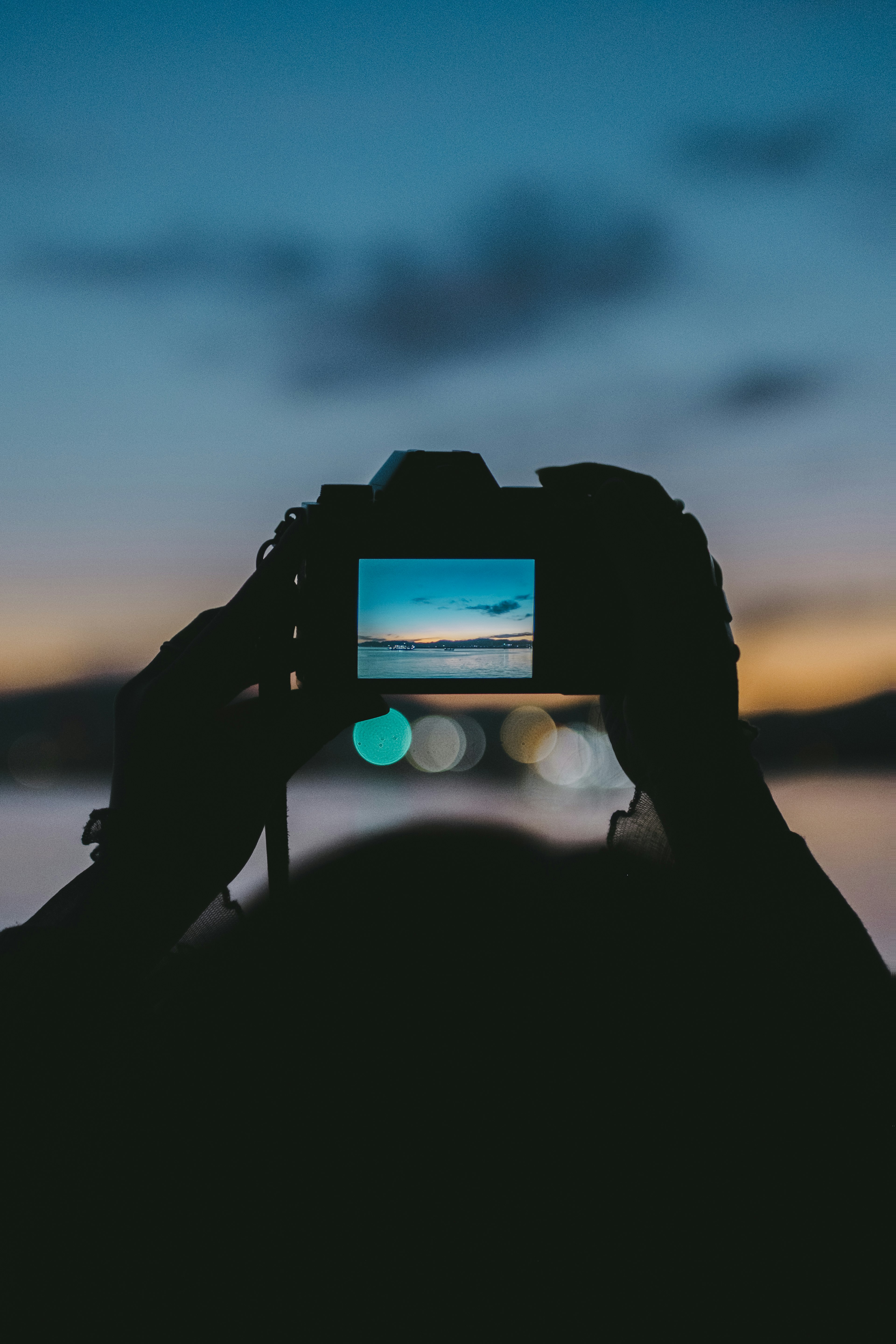 夕焼けの空を撮影しているカメラマンのシルエットとカメラの液晶画面に映る風景