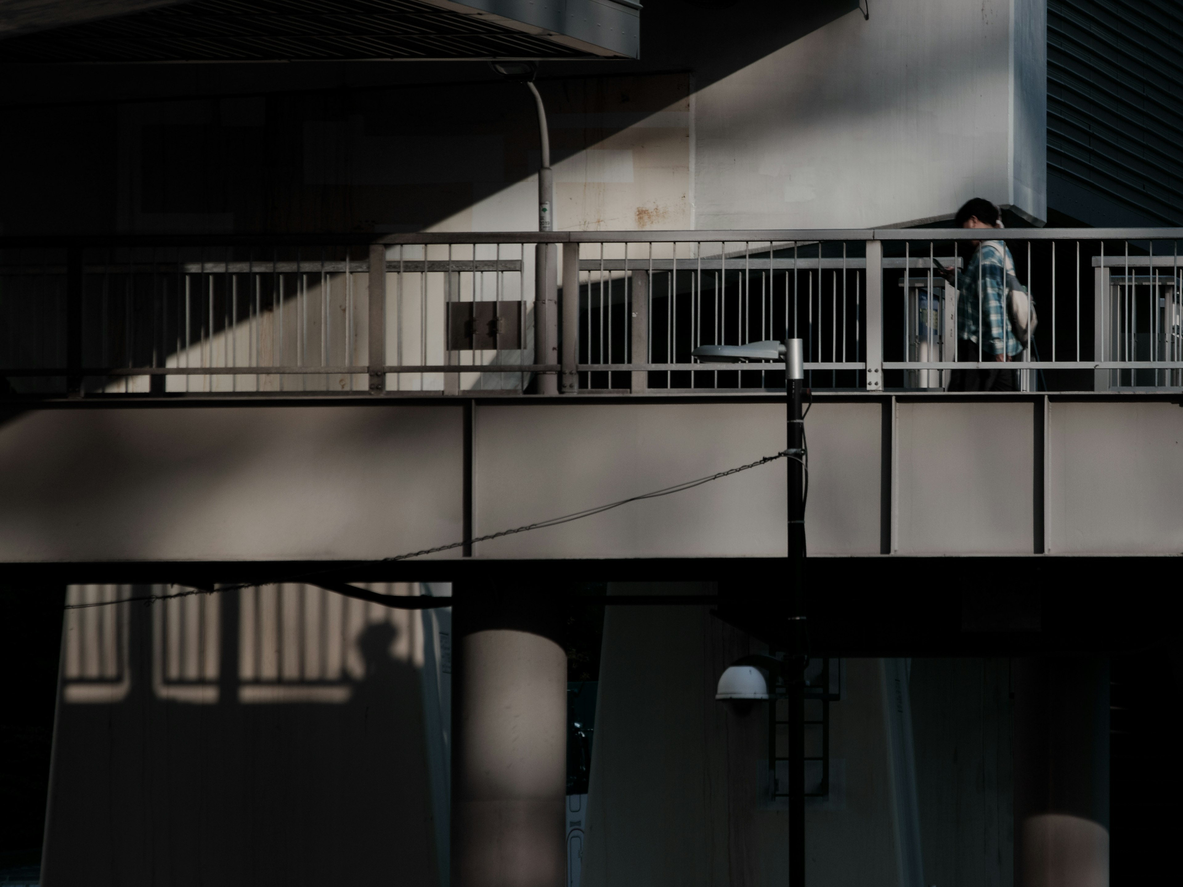 A person walking on an urban overpass highlighted by contrasting shadows and light