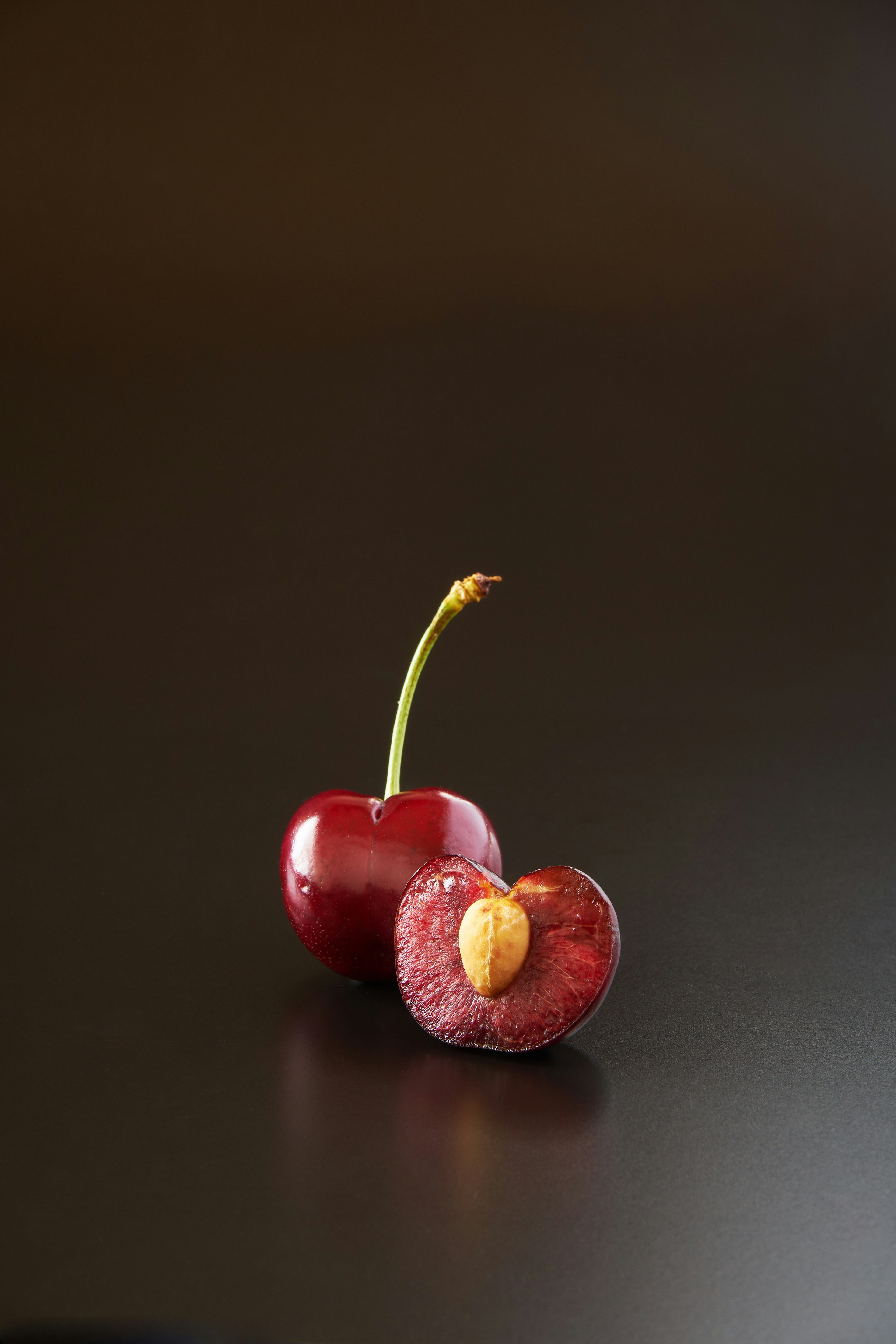 A red cherry with a cut revealing its seed on a dark background