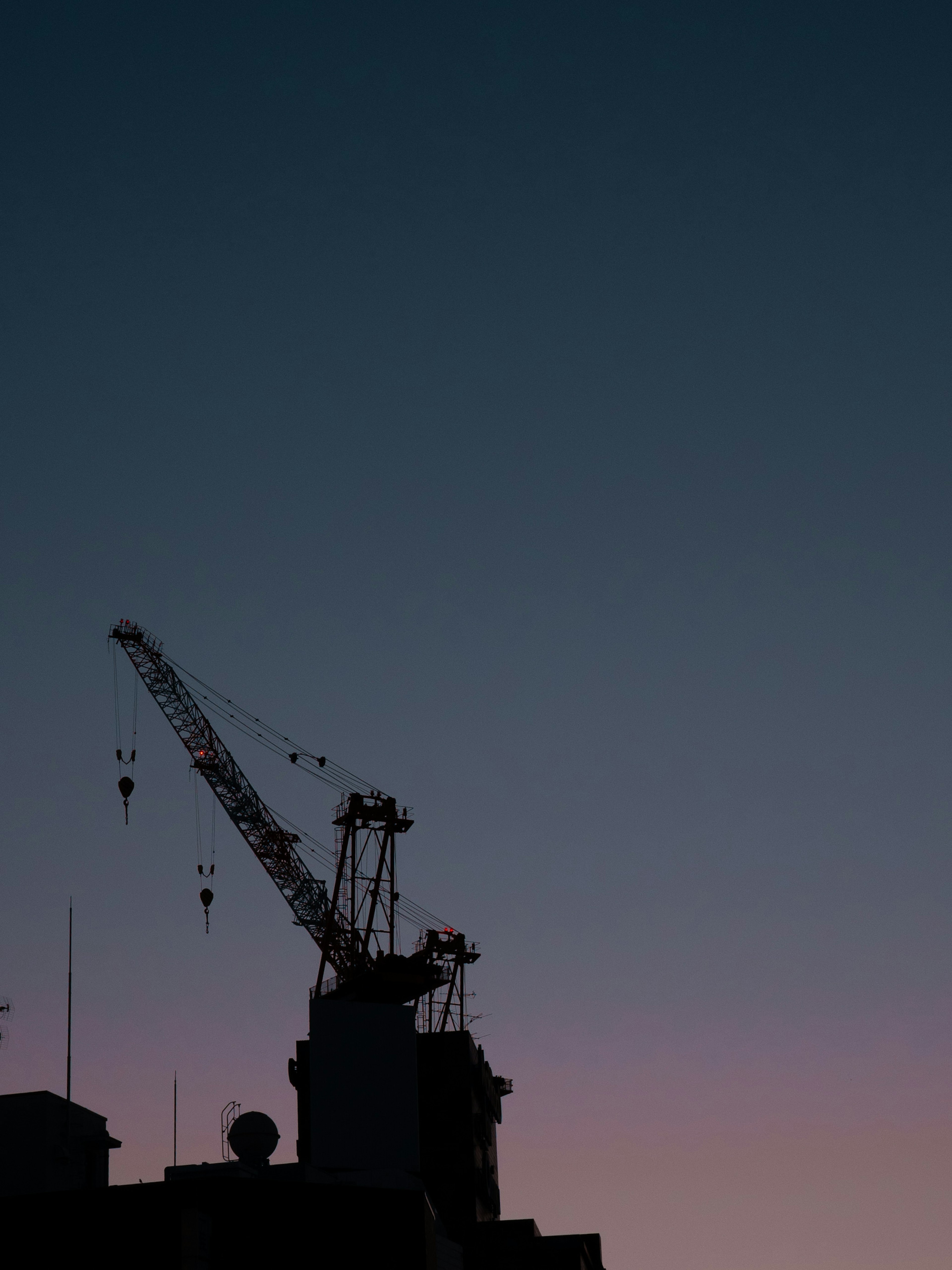 Silhouette di una gru contro un cielo al tramonto con contorni di edifici