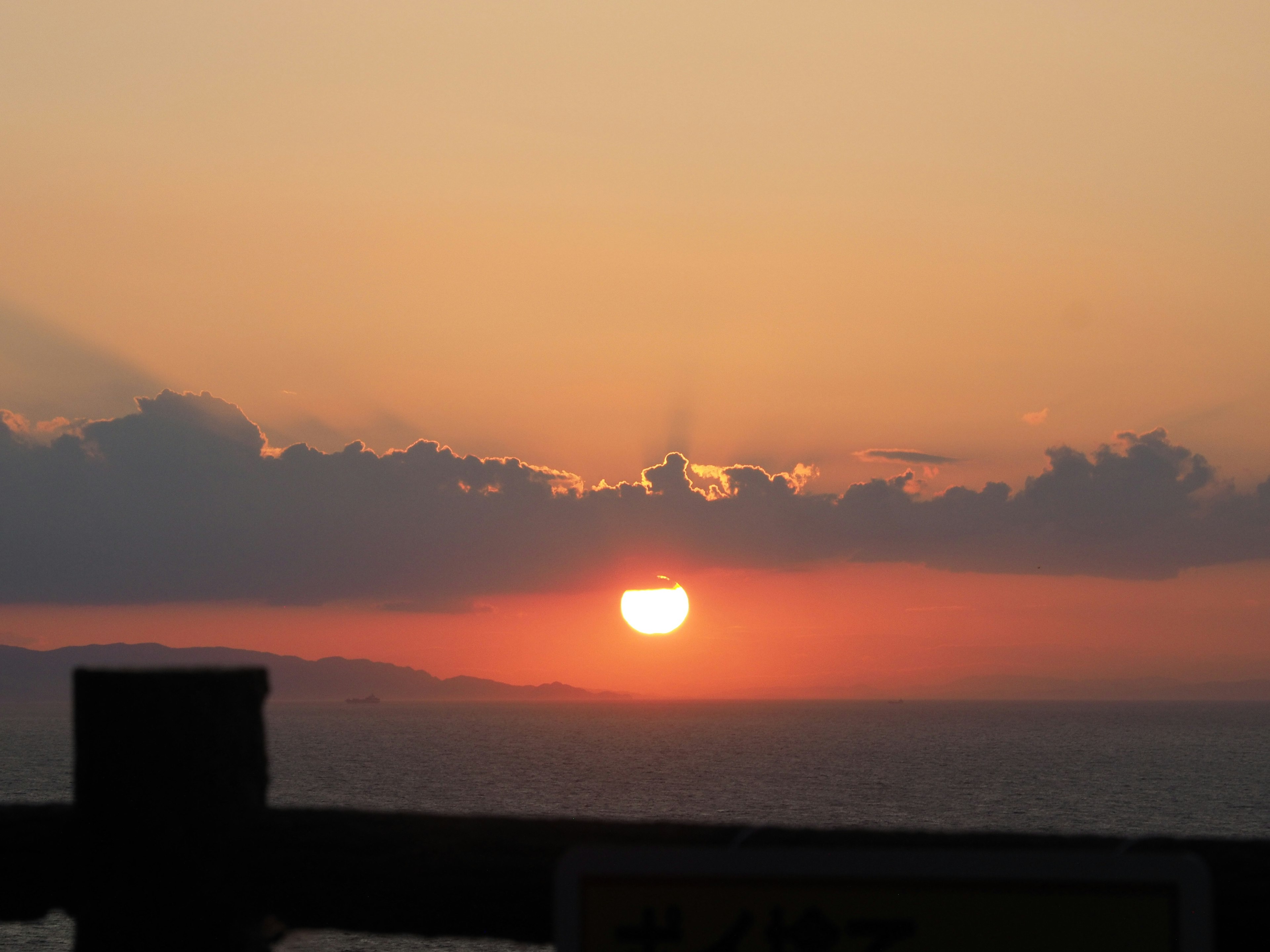 夕日の美しい風景で、オレンジ色とピンク色の空が広がり、雲の間から太陽が見える