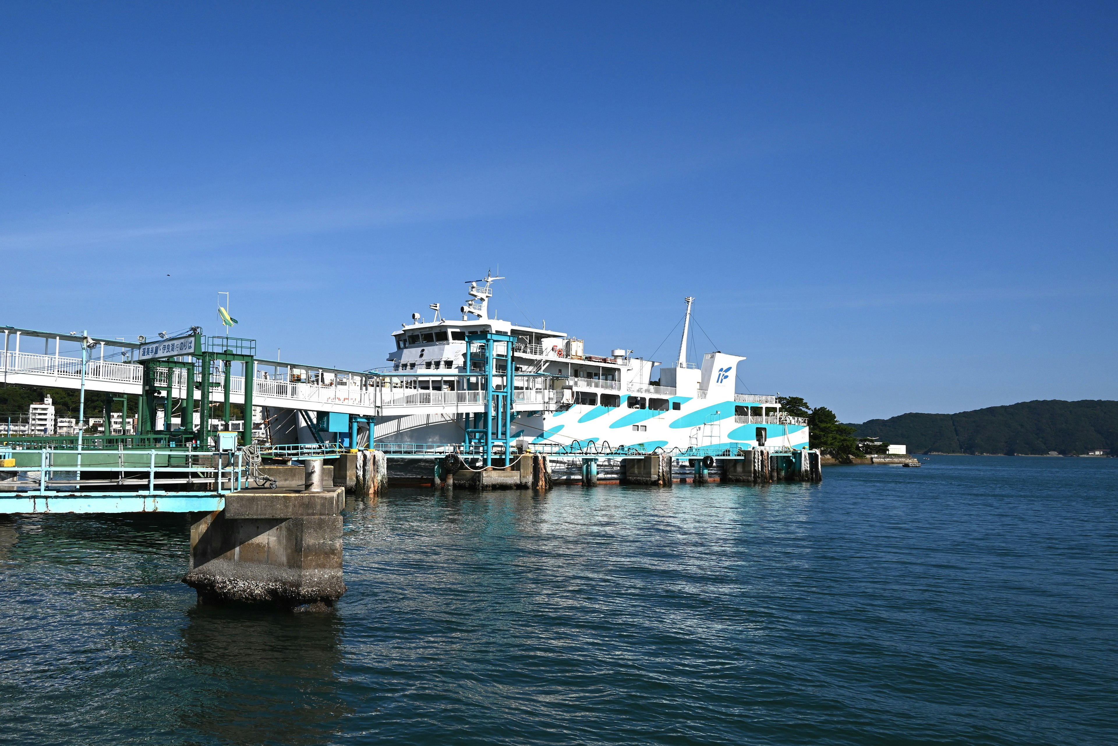 A blue ferry docked at a harbor under a clear blue sky