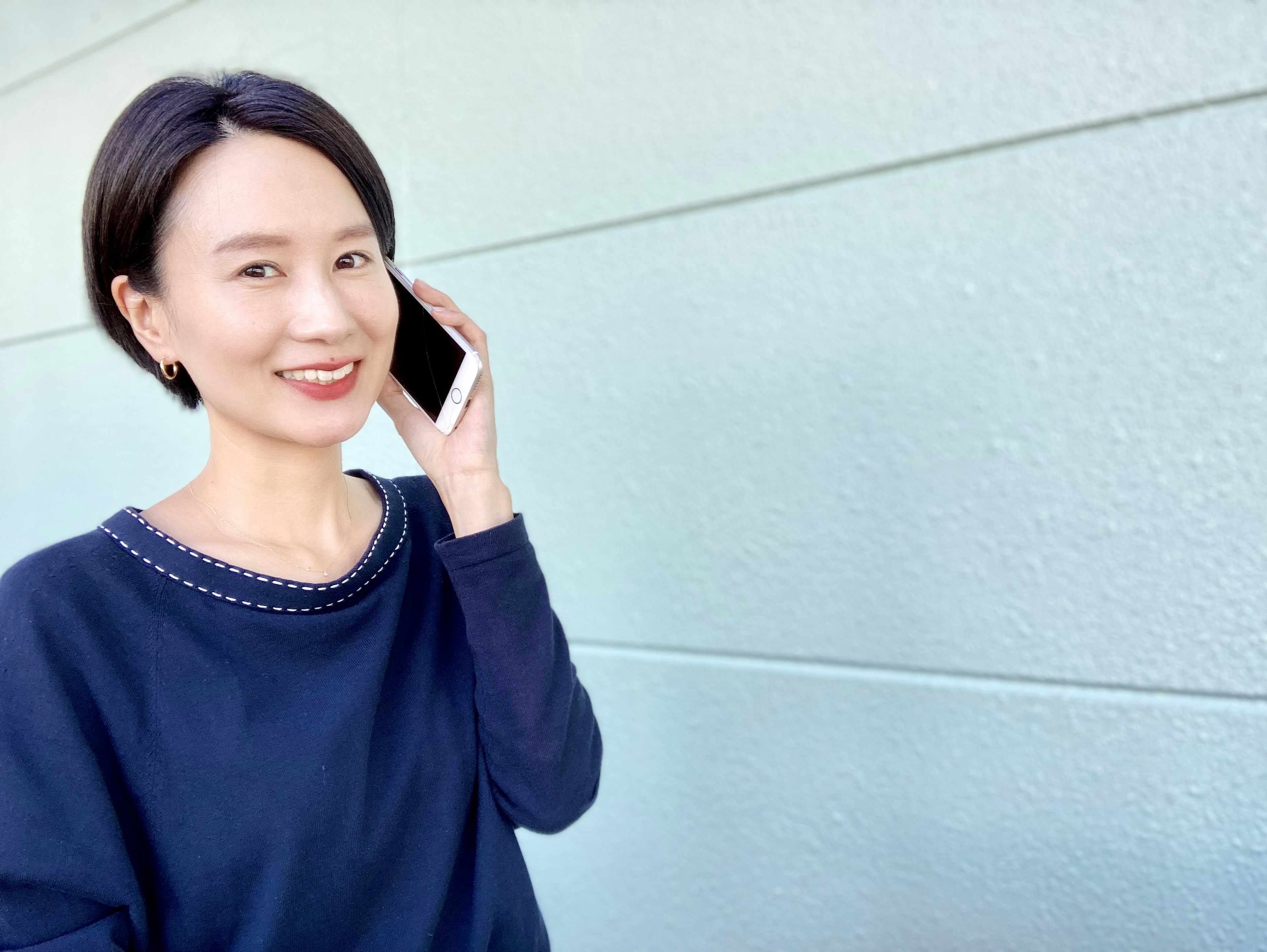 Woman smiling while holding a smartphone in front of a blue wall