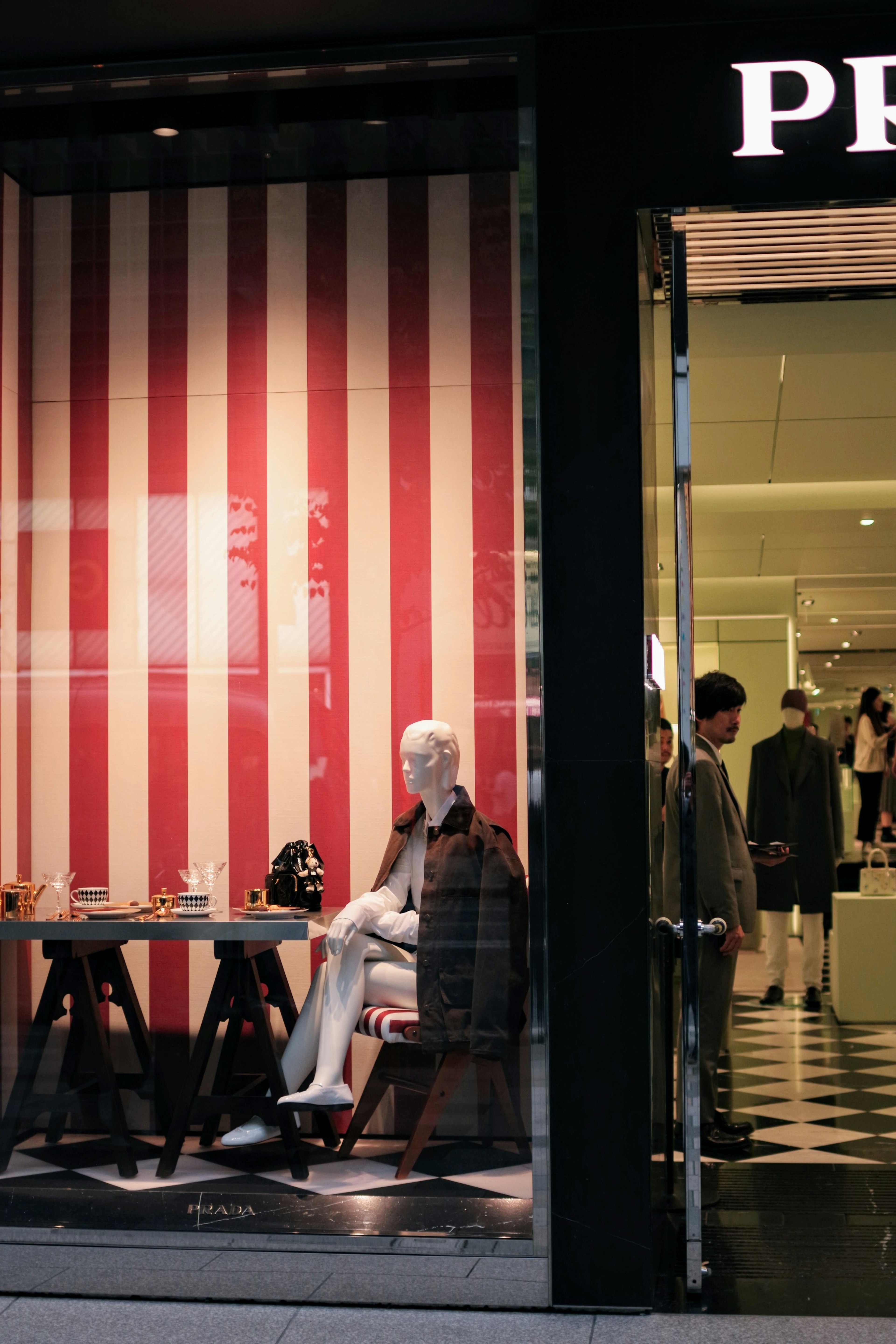 A mannequin seated in front of red and white striped wall with a stylish interior