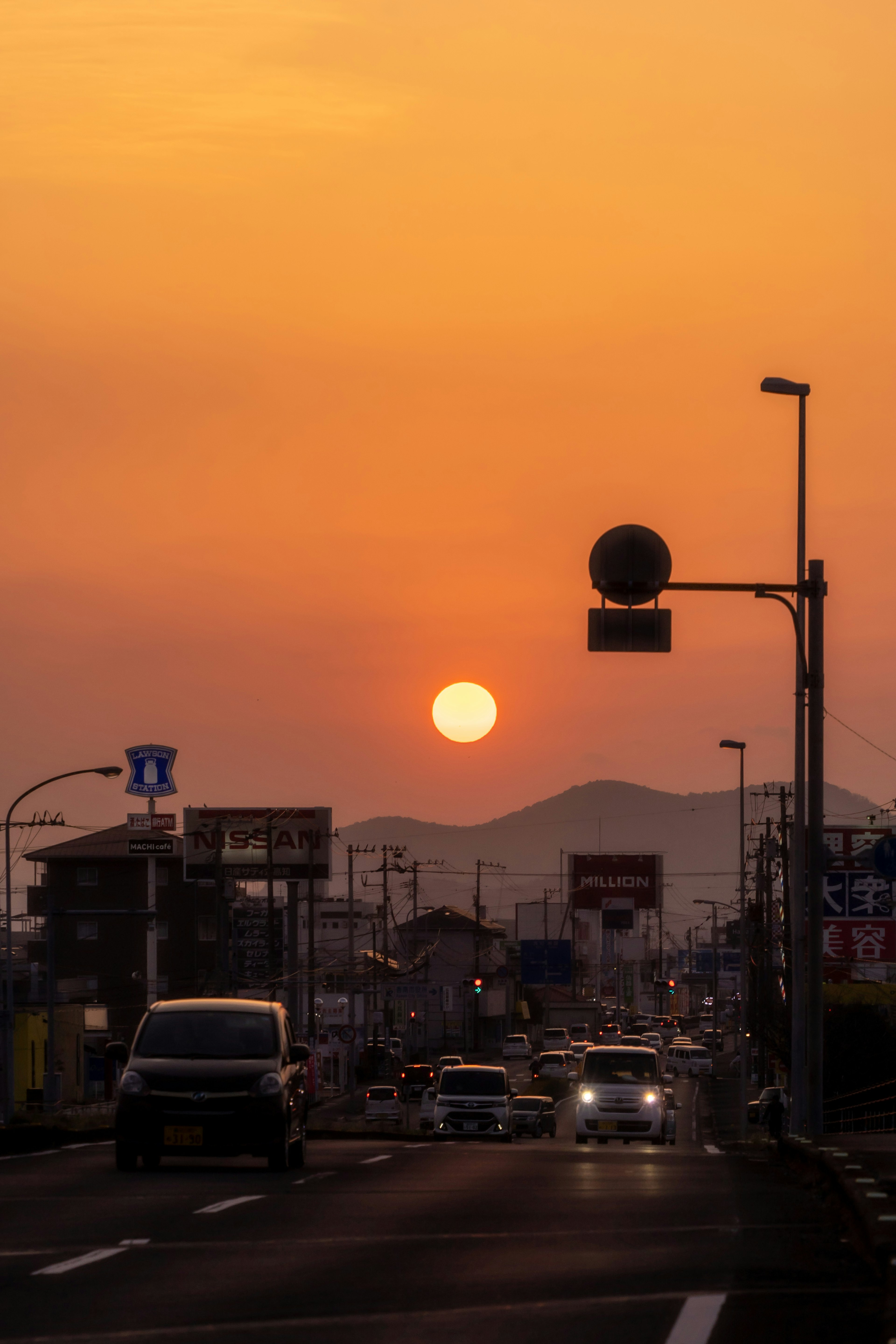 オレンジ色の夕日が沈む街の風景車が走る道路