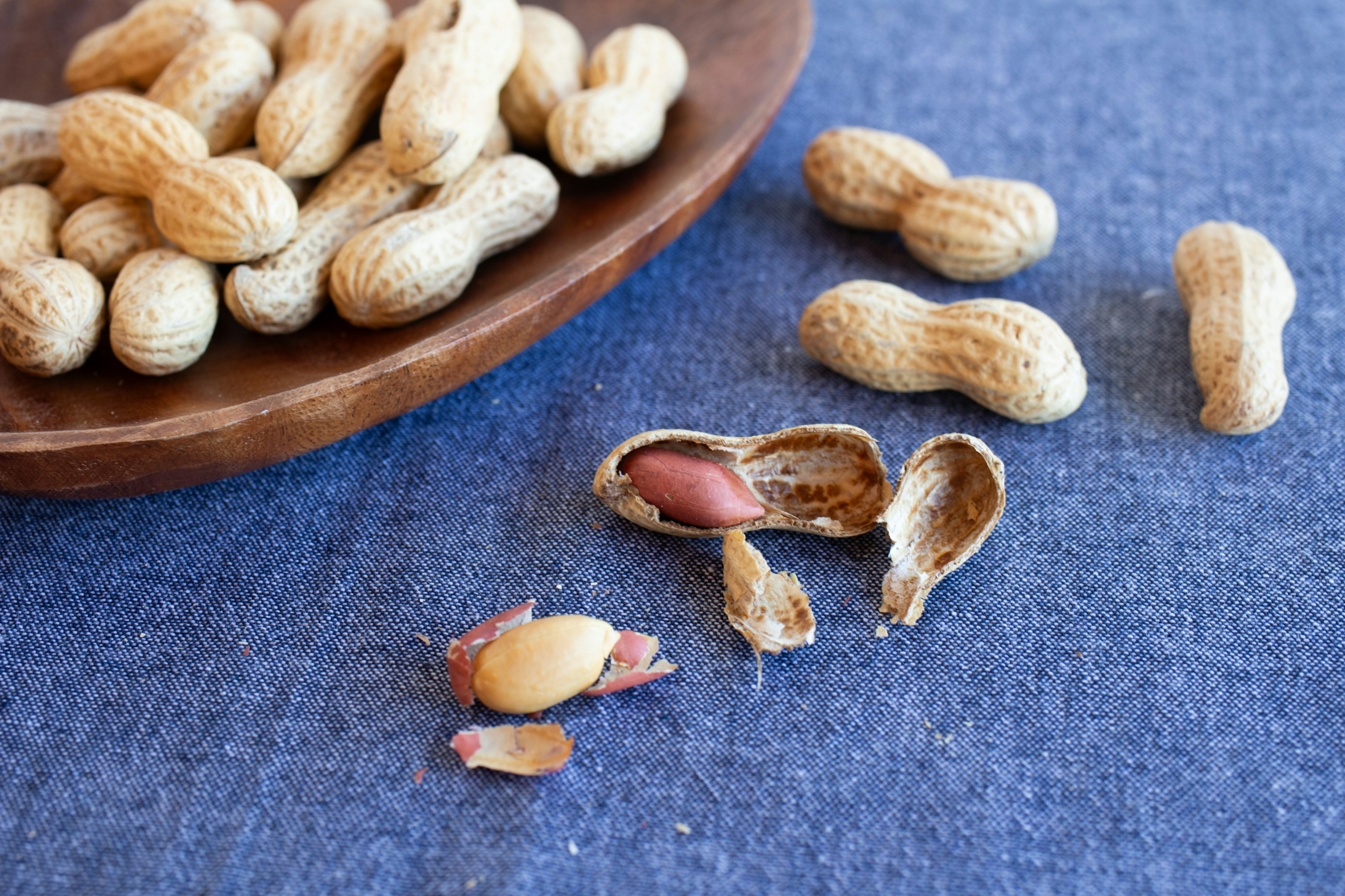 Kacang tanah yang tersebar di atas kain biru dengan mangkuk kayu berisi kacang tanah