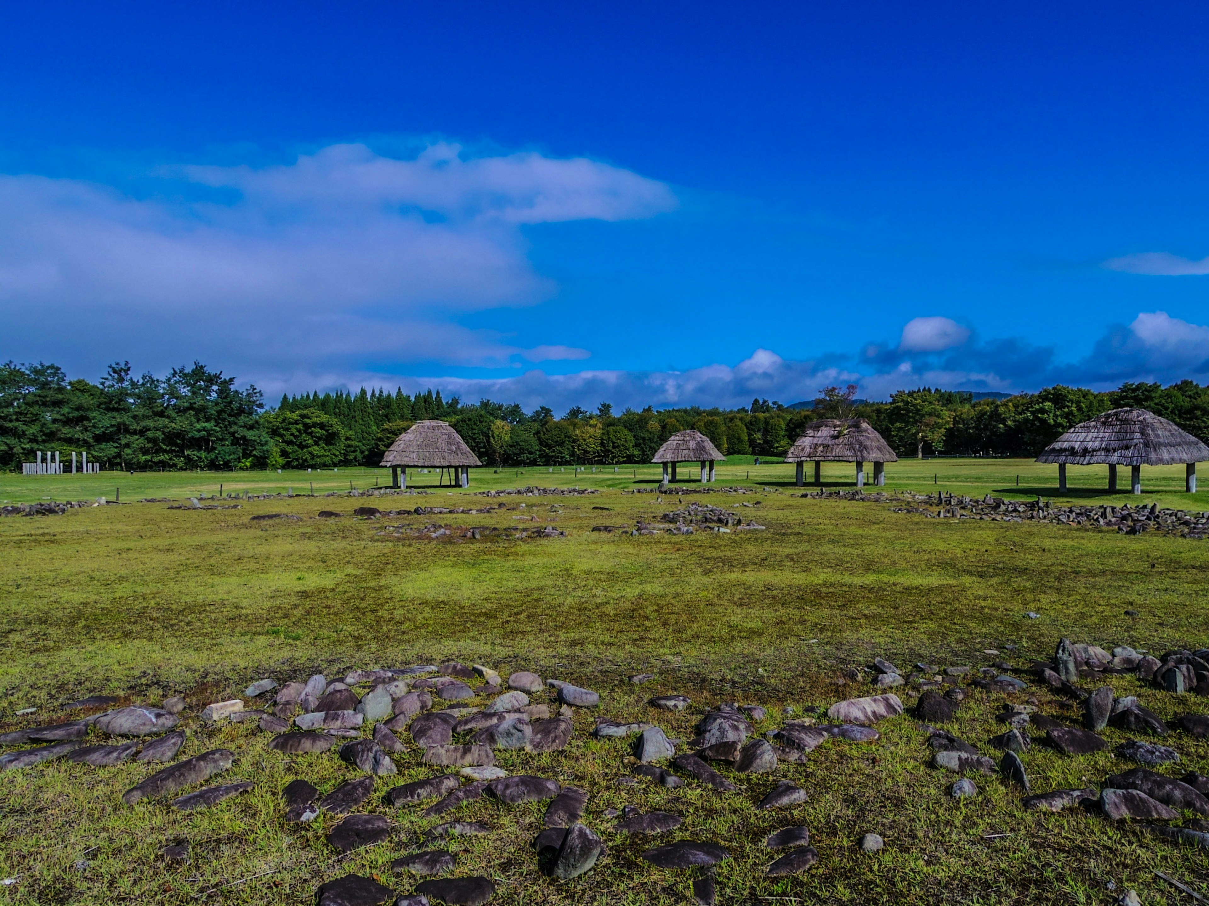 Paisaje con cabañas de paja en un terreno cubierto de hierba bajo un cielo azul