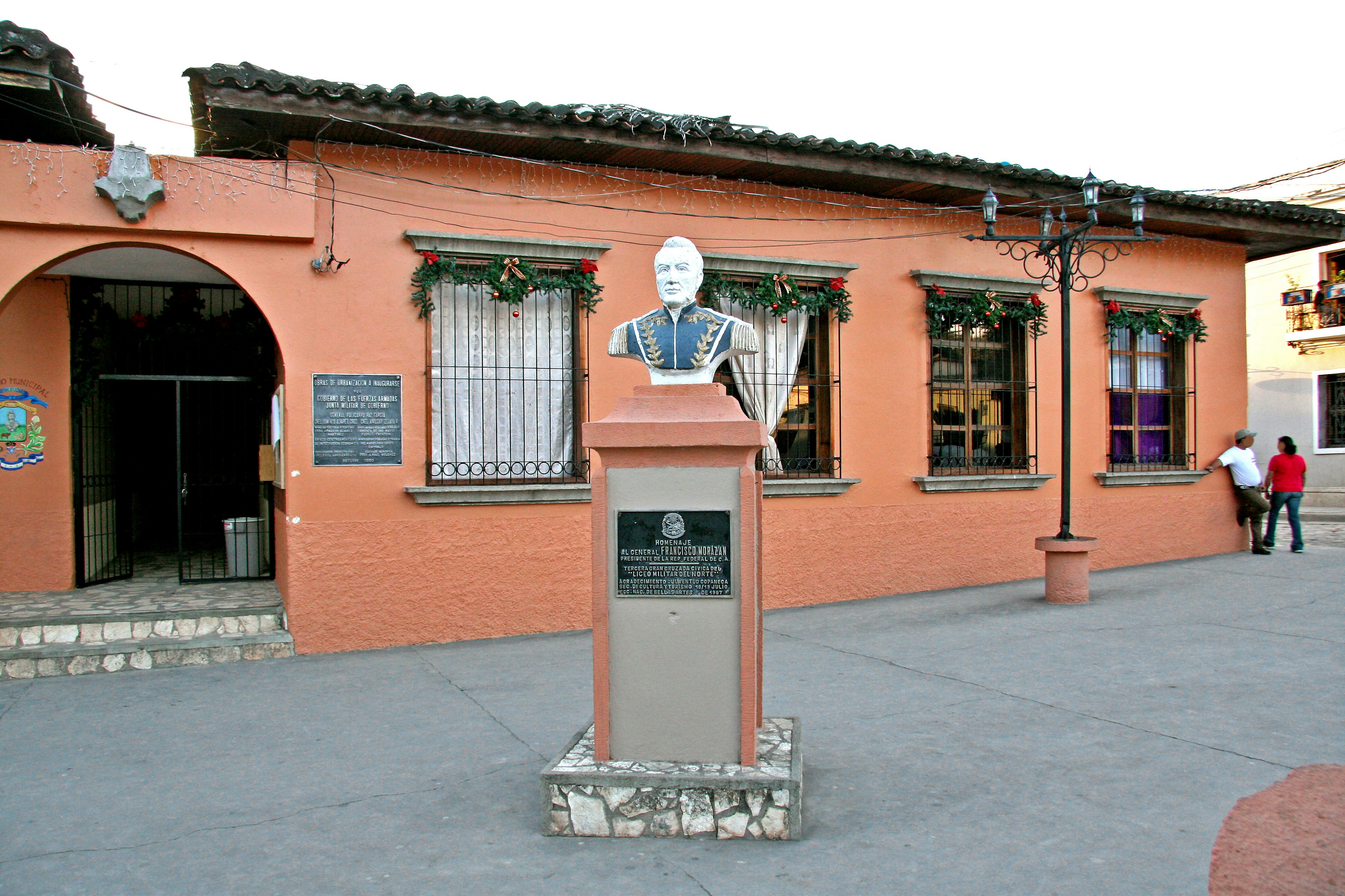 Orange building with a statue in front and people walking nearby