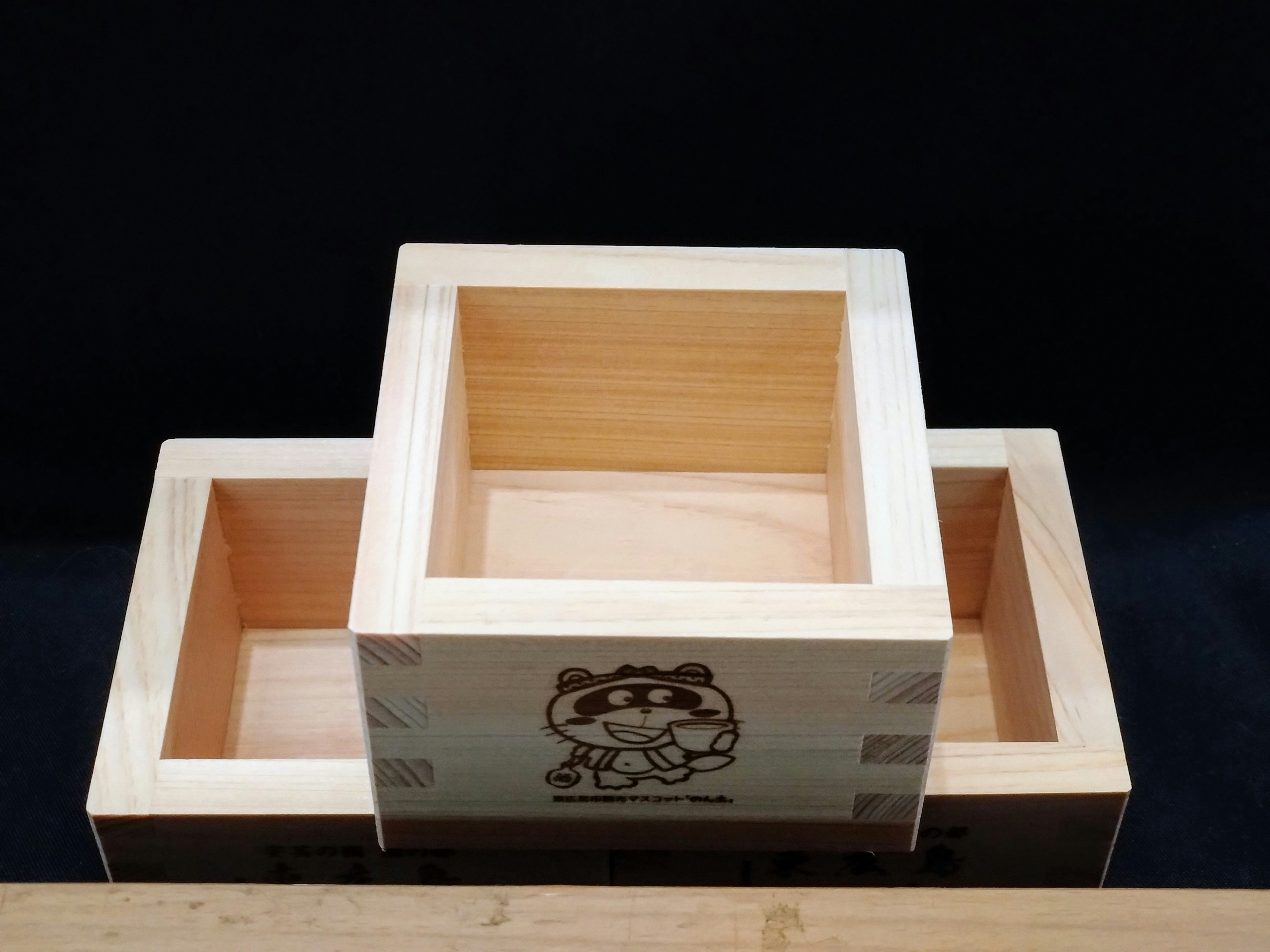 Three wooden masu boxes stacked on top of each other with a black background