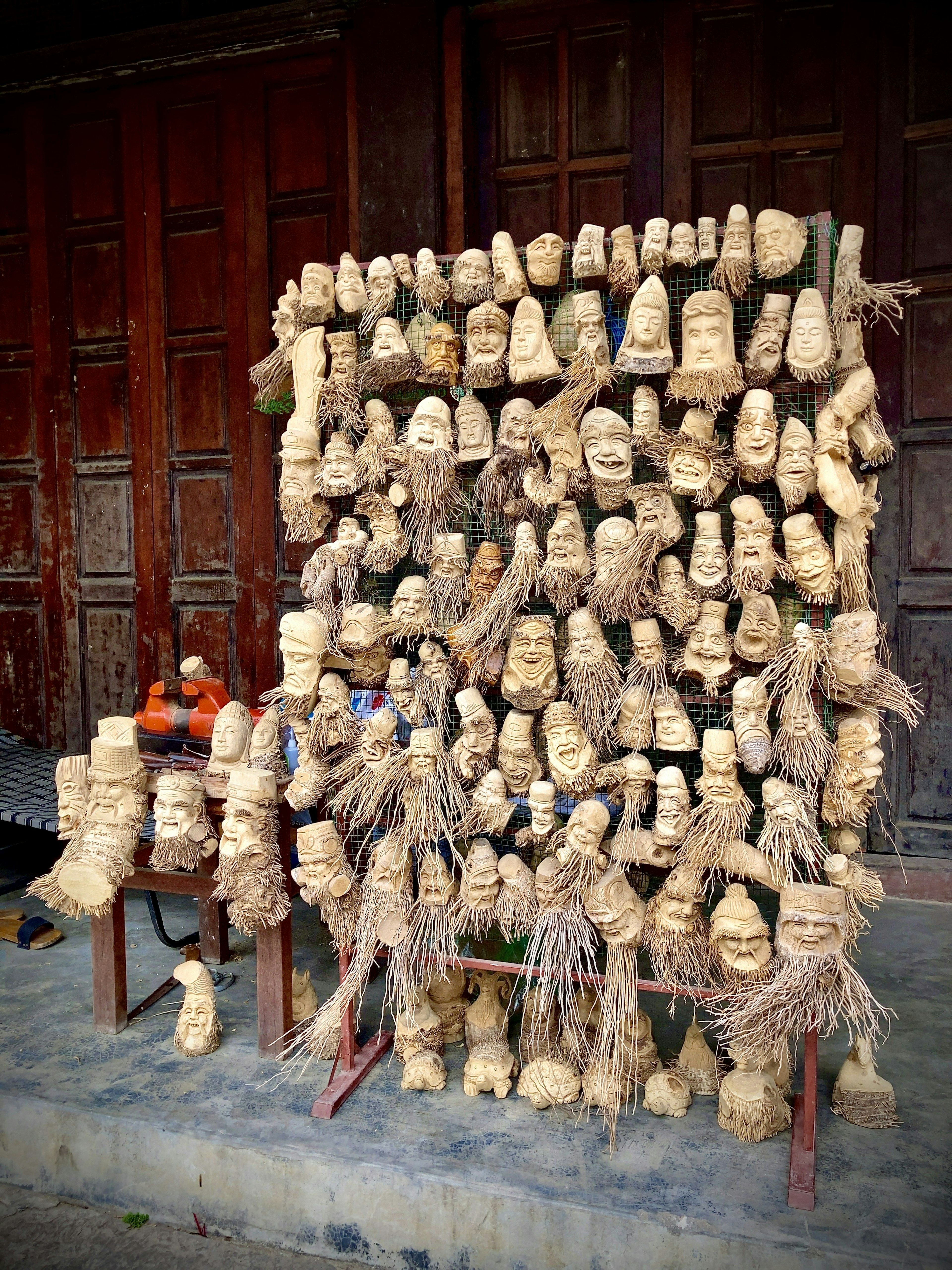 Exhibición de esculturas de madera y máscaras dispuestas en una pared