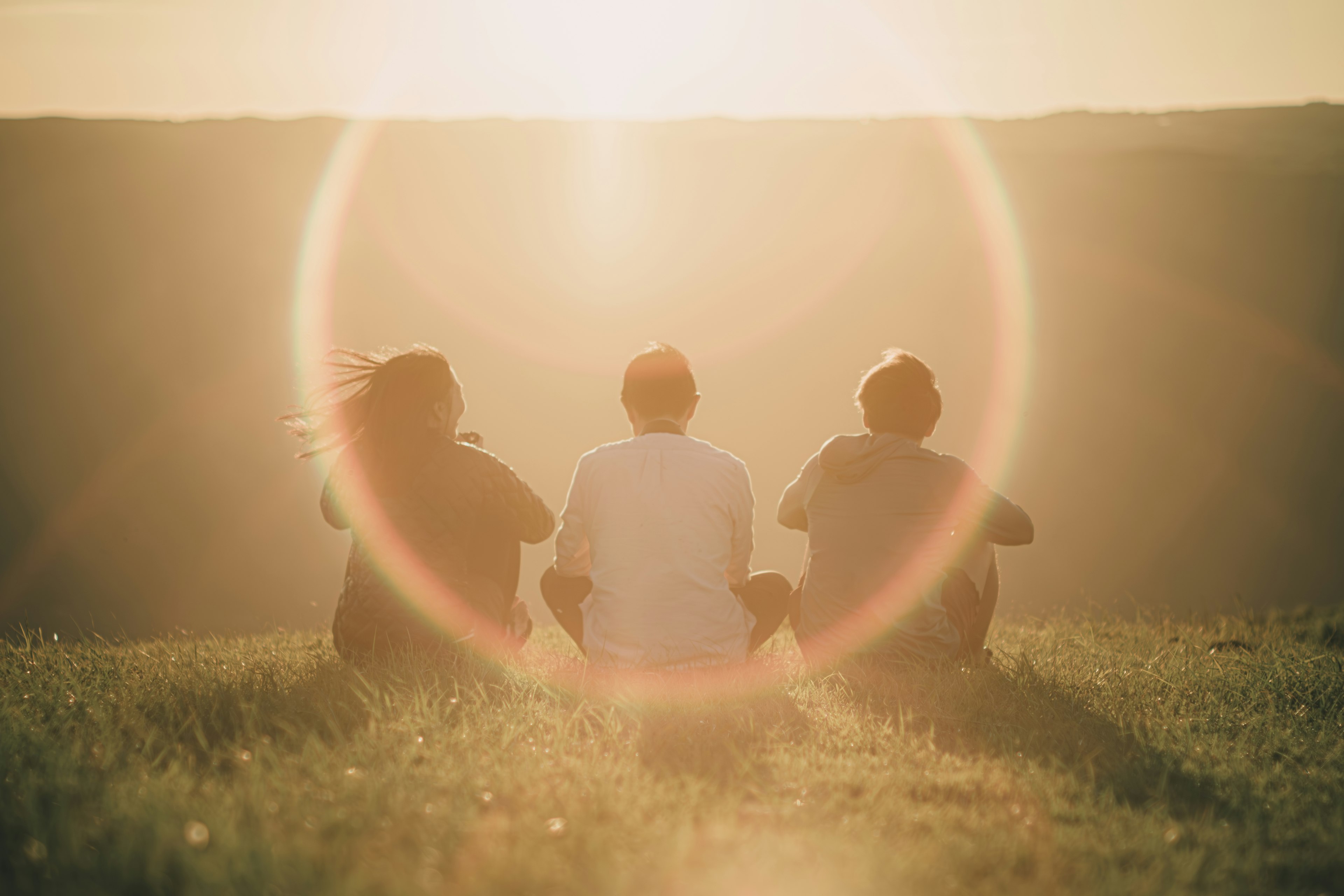 Silhouette von drei Personen, die den Sonnenuntergang mit einem Halo-Effekt beobachten