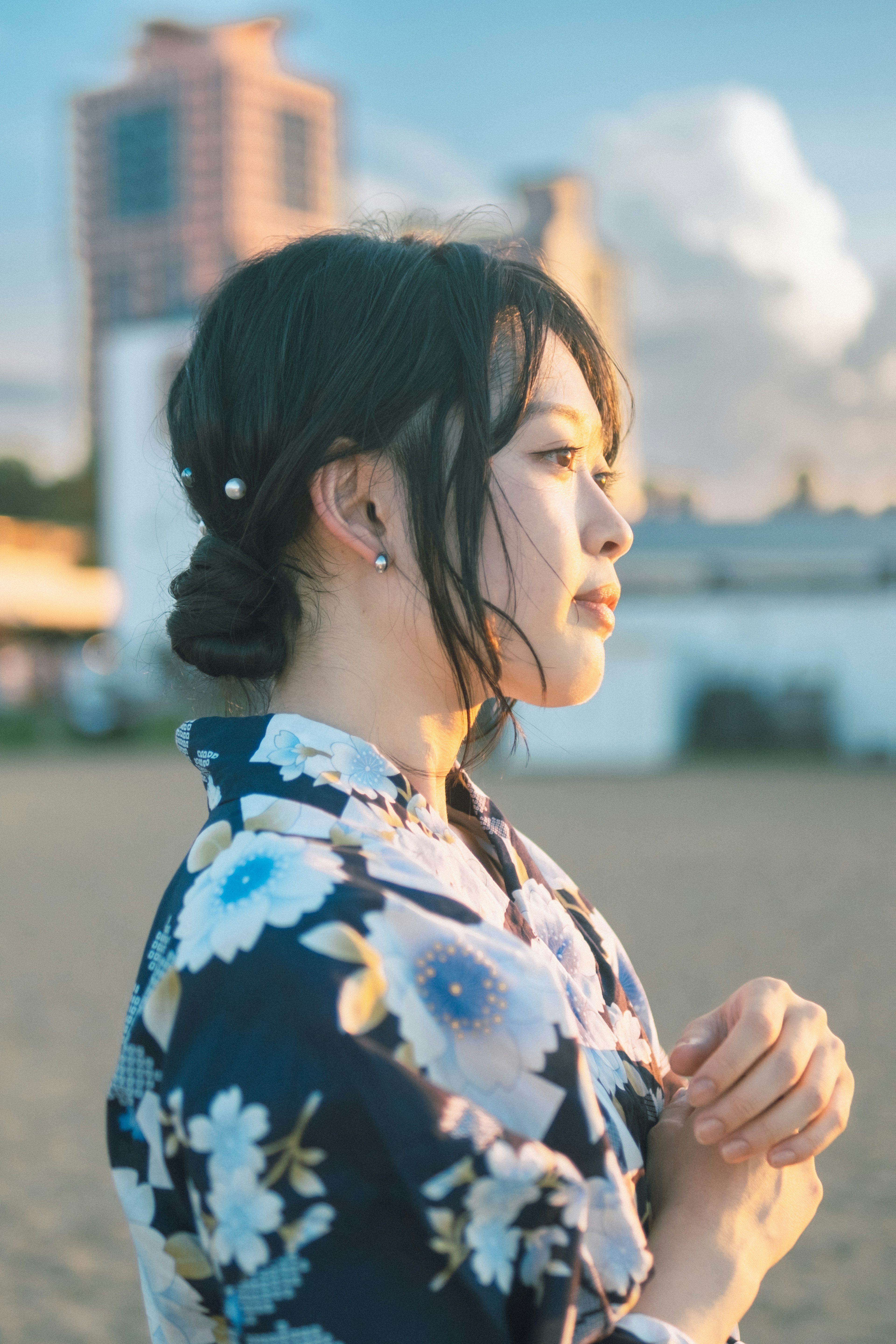 Wanita mengenakan yukata floral berdiri menyamping dengan langit biru dan bangunan di latar belakang