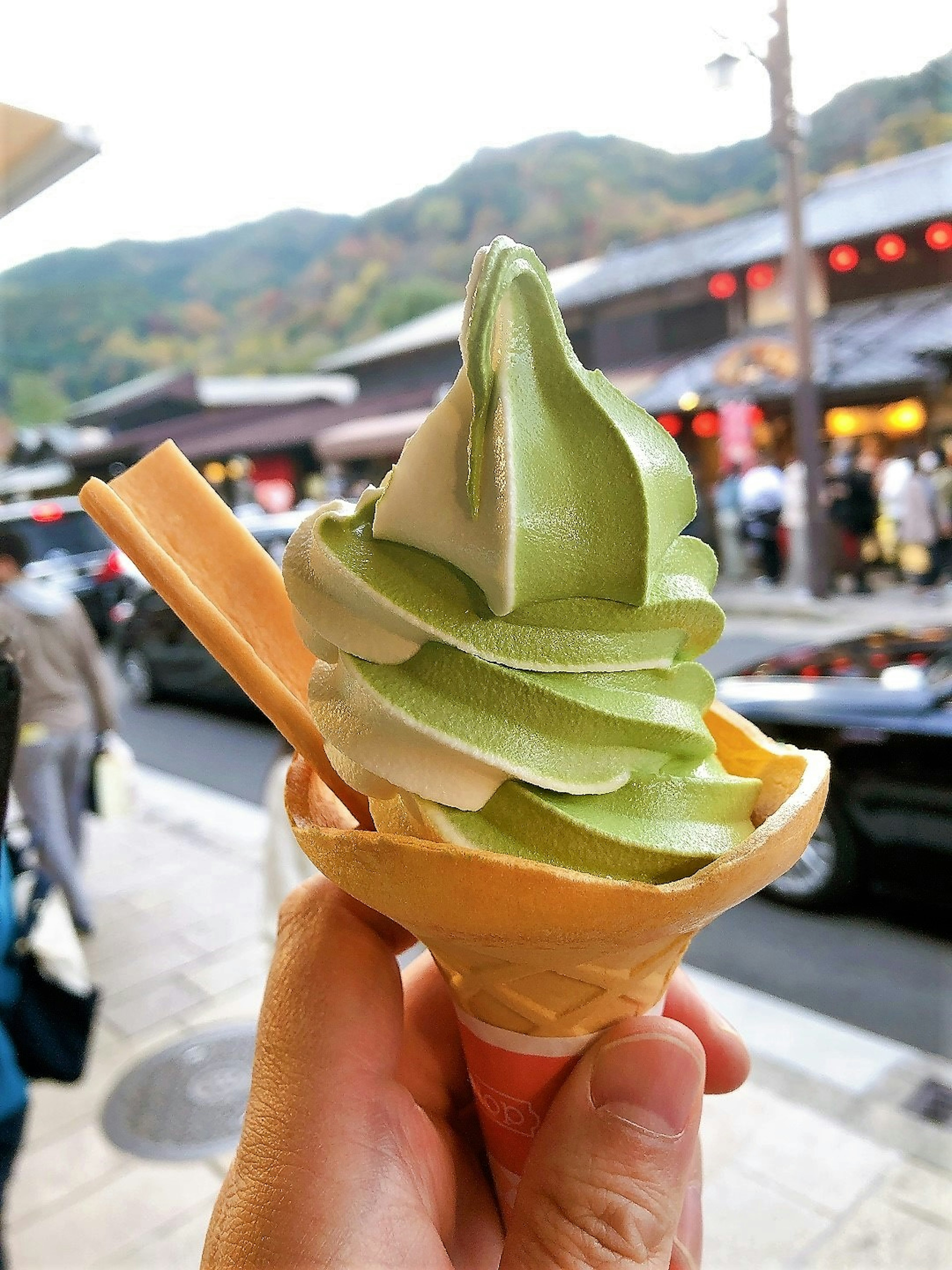 Mano sosteniendo un cono de helado de té verde con montañas al fondo