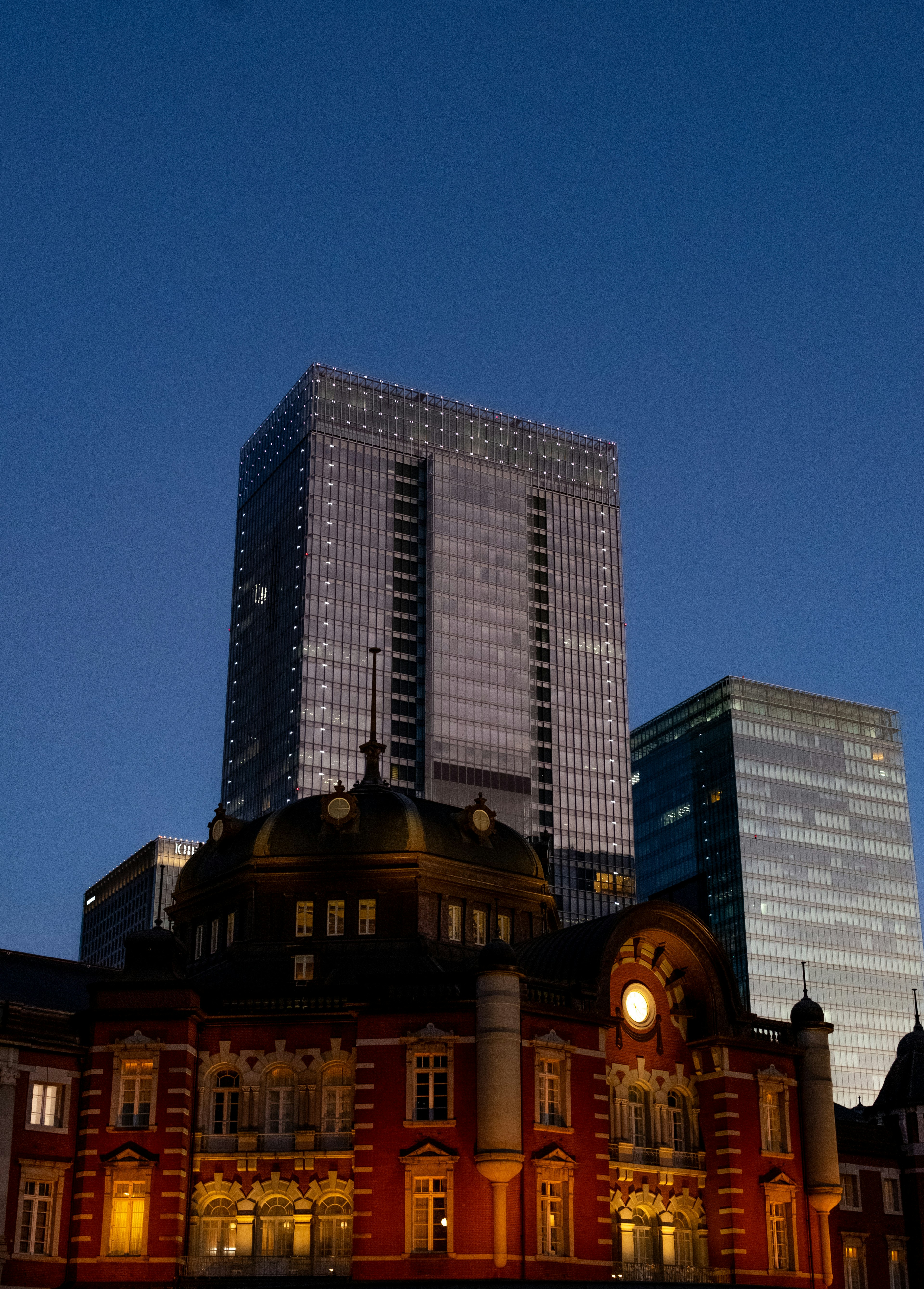 Vue nocturne montrant la gare historique de Tokyo avec des gratte-ciels modernes en arrière-plan