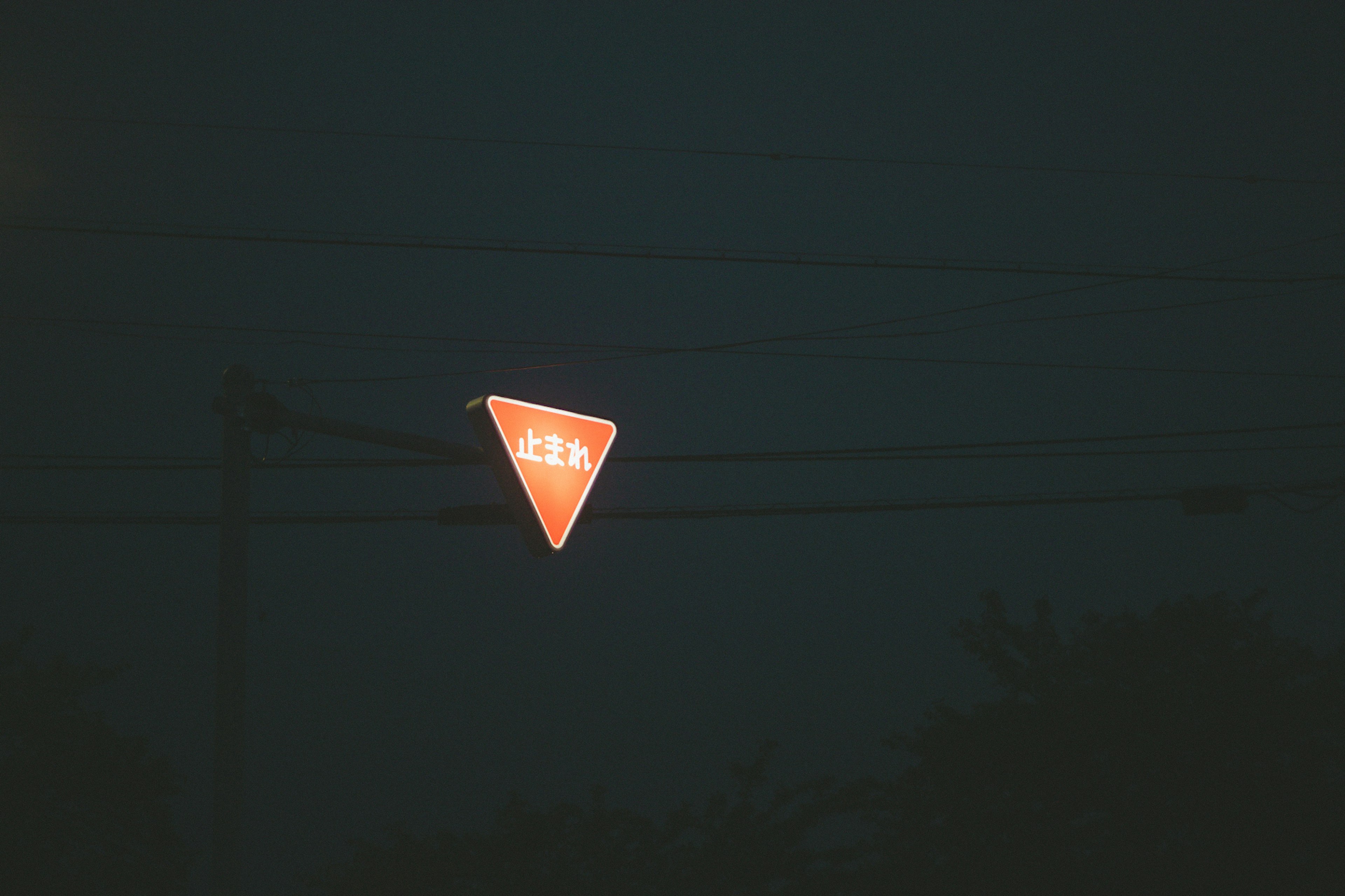 Orange triangular traffic sign illuminated against a dark background