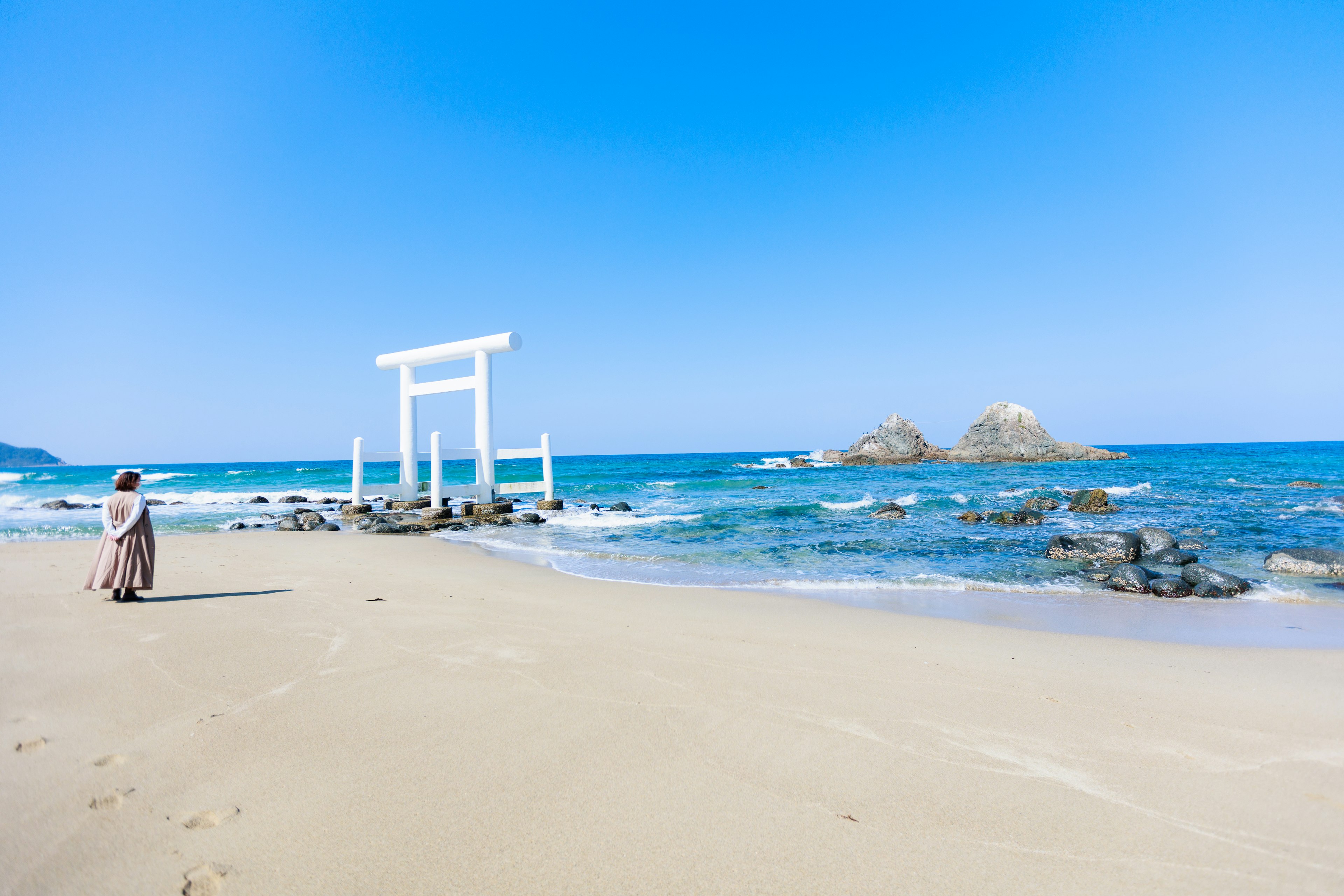 海辺に立つ白い鳥居と女性のシルエットのある風景