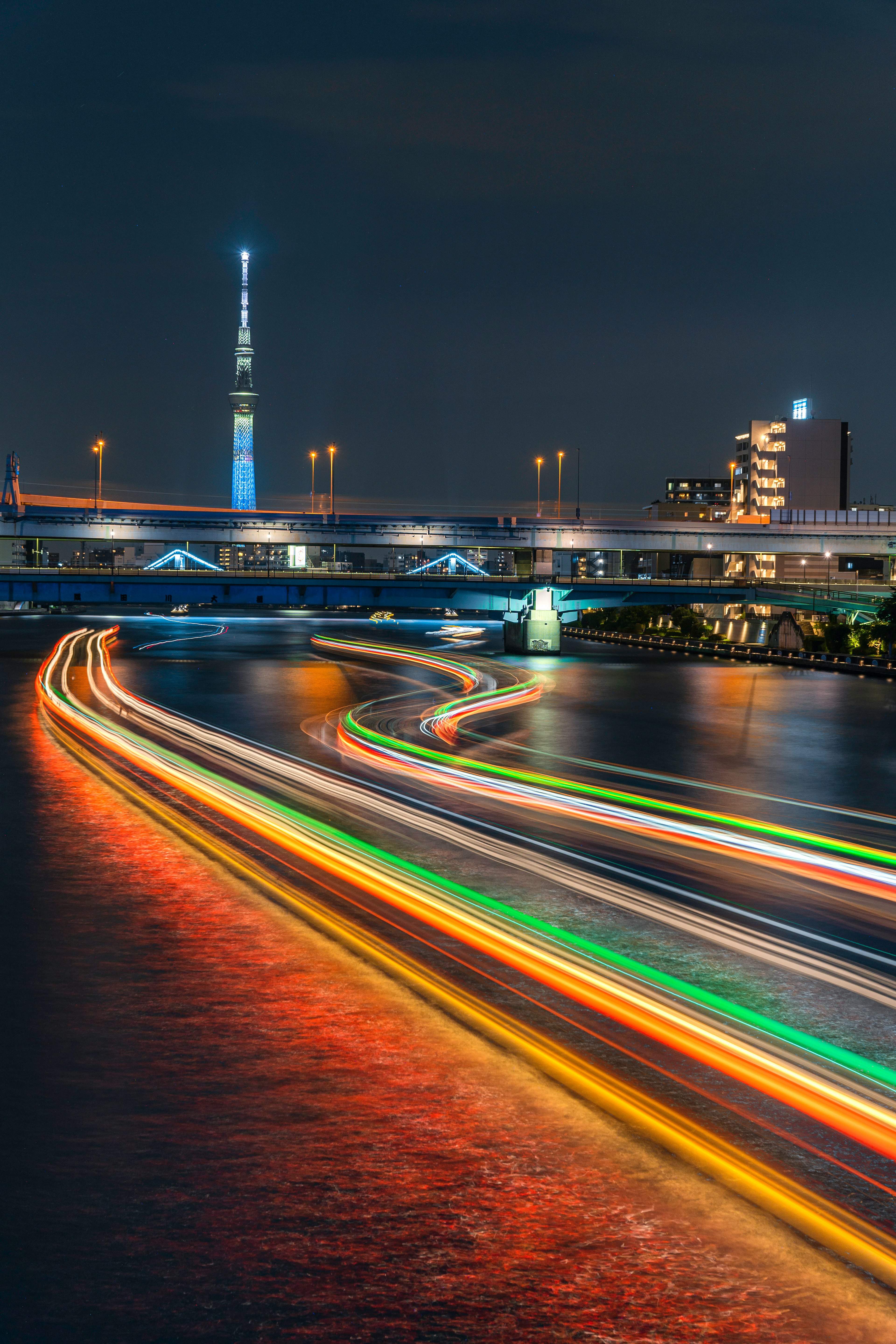 夜の東京スカイツリーと流れる光の軌跡が映る川の風景