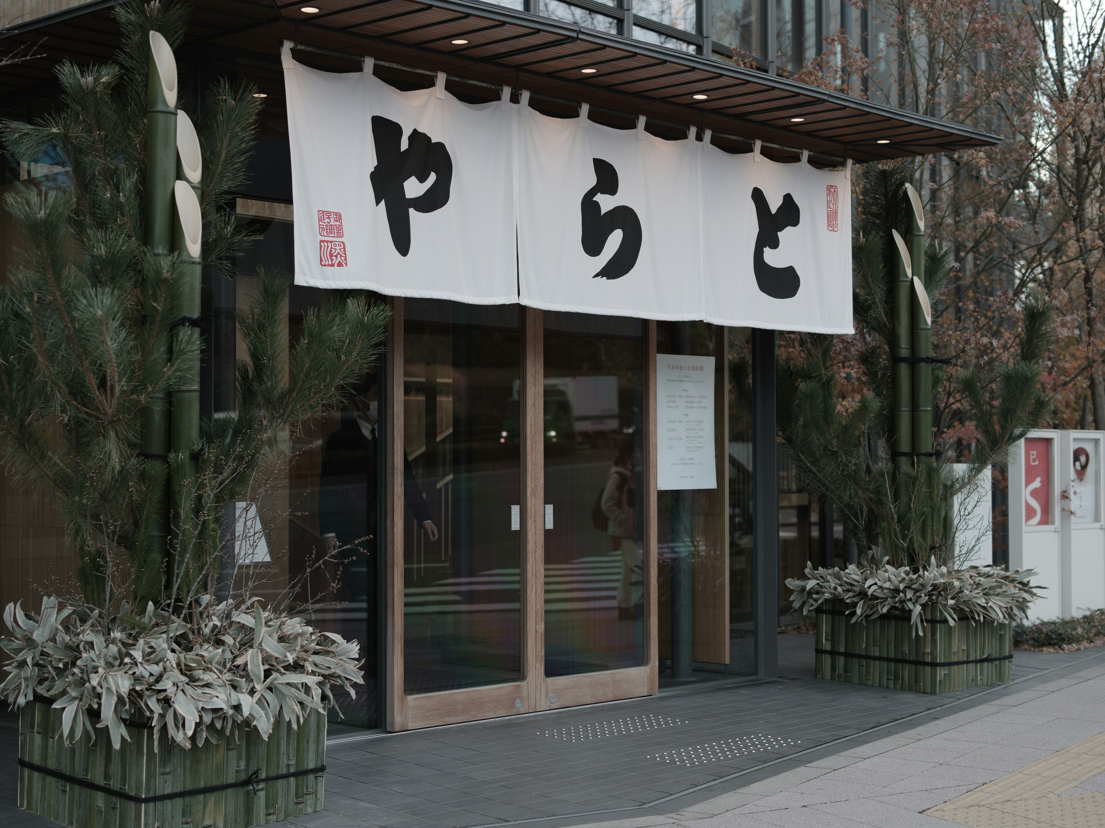 Entrada de un restaurante japonés con un noren blanco y plantas verdes