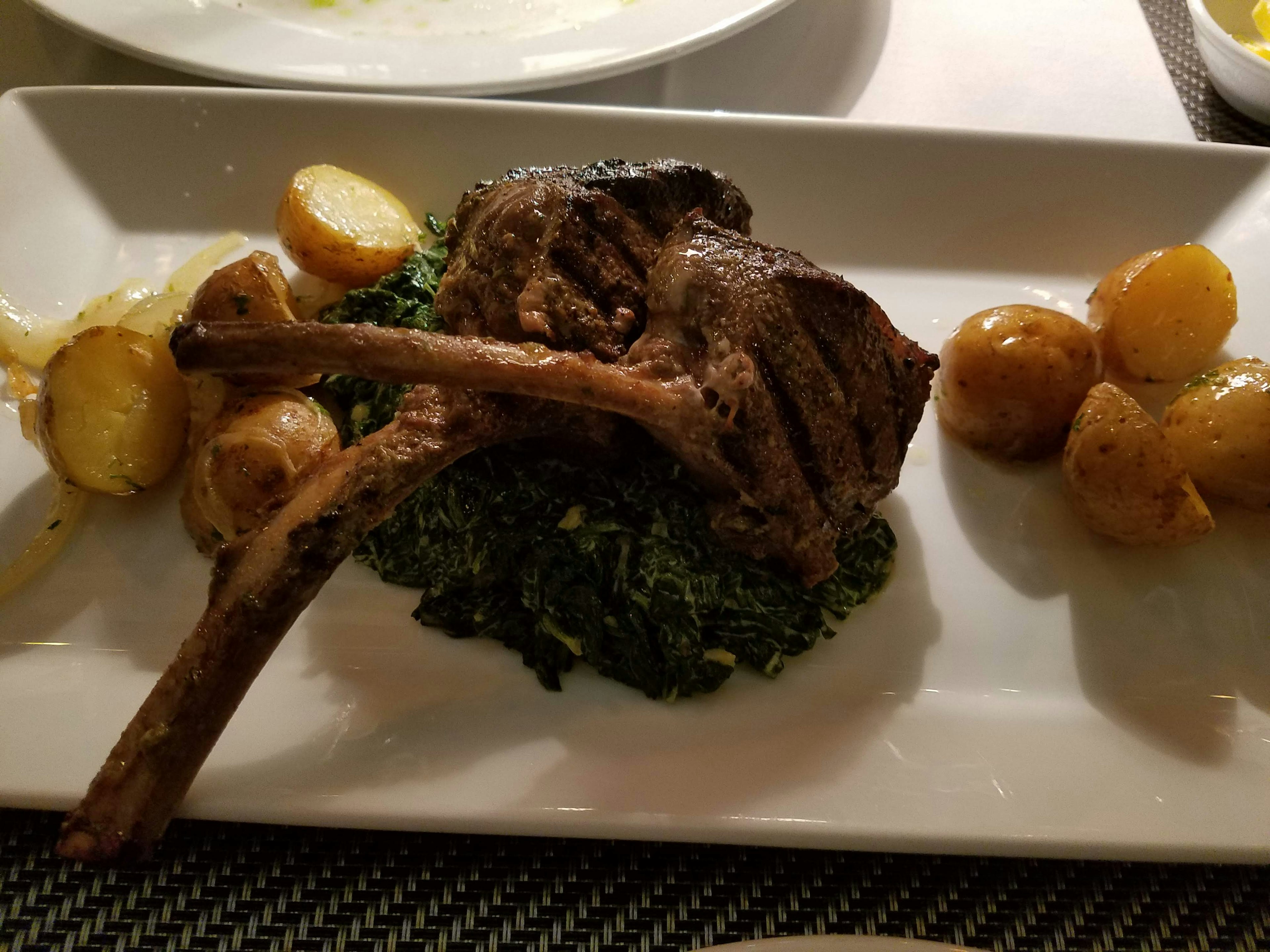 A grilled lamb chop on a bed of greens with roasted potatoes