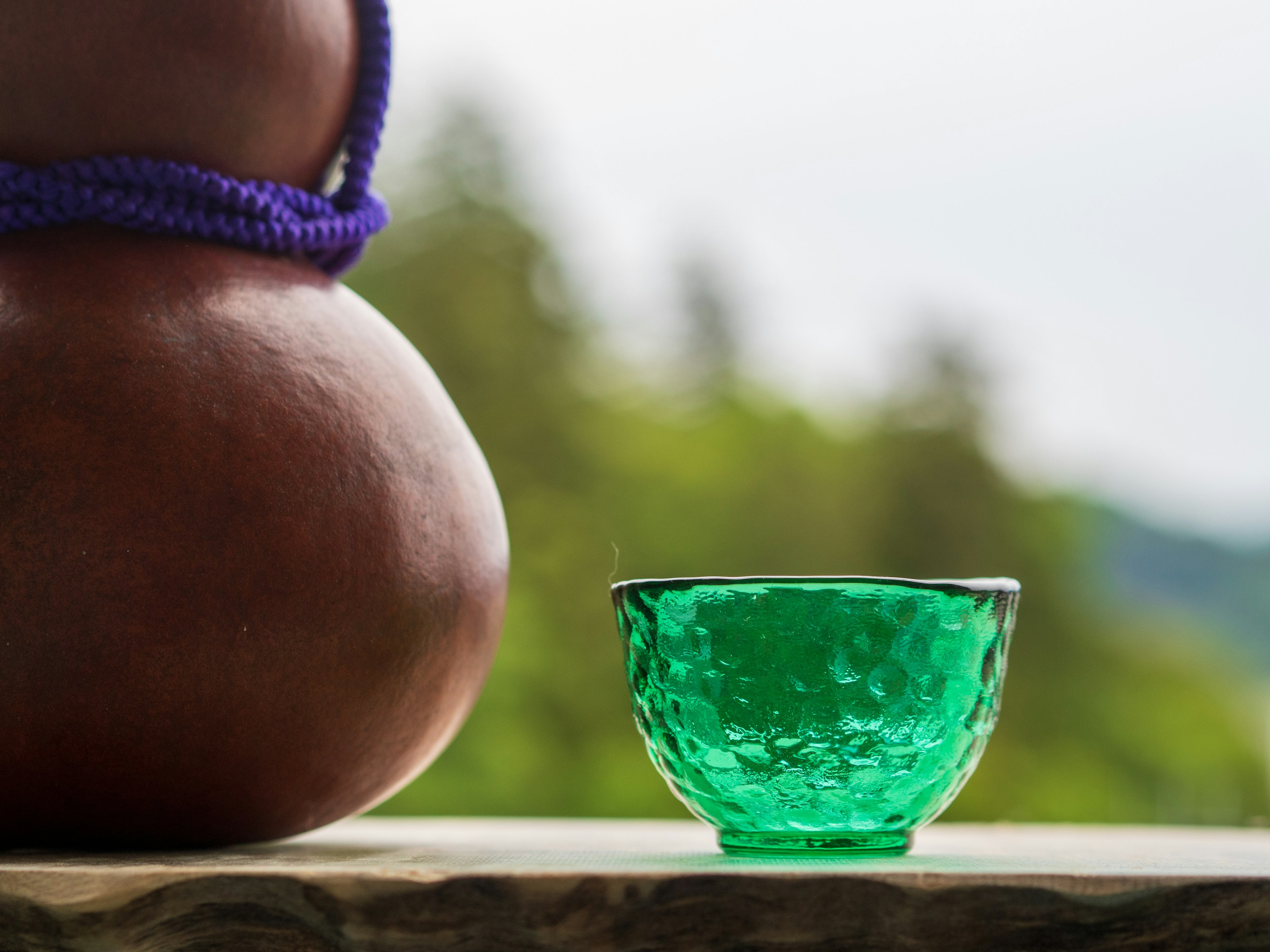 Un bol en verre vert à côté d'une gourde marron avec une corde violette