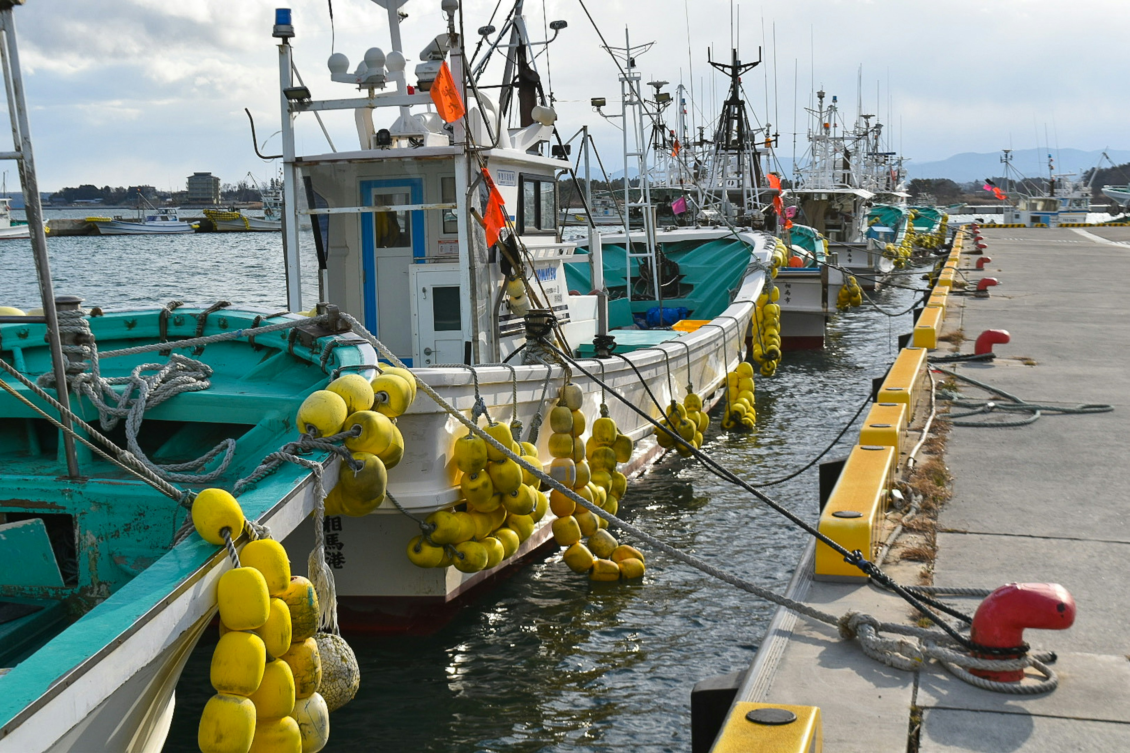 Barcos de pesca atracados en un puerto con boyas amarillas colgando de las embarcaciones