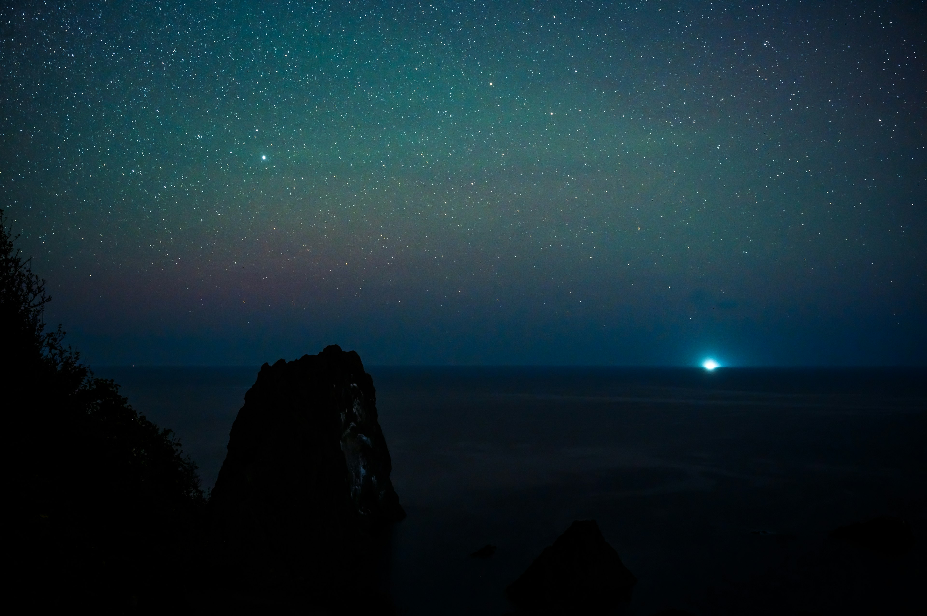 Silhouette de rochers sombres sous un ciel étoilé et l'océan