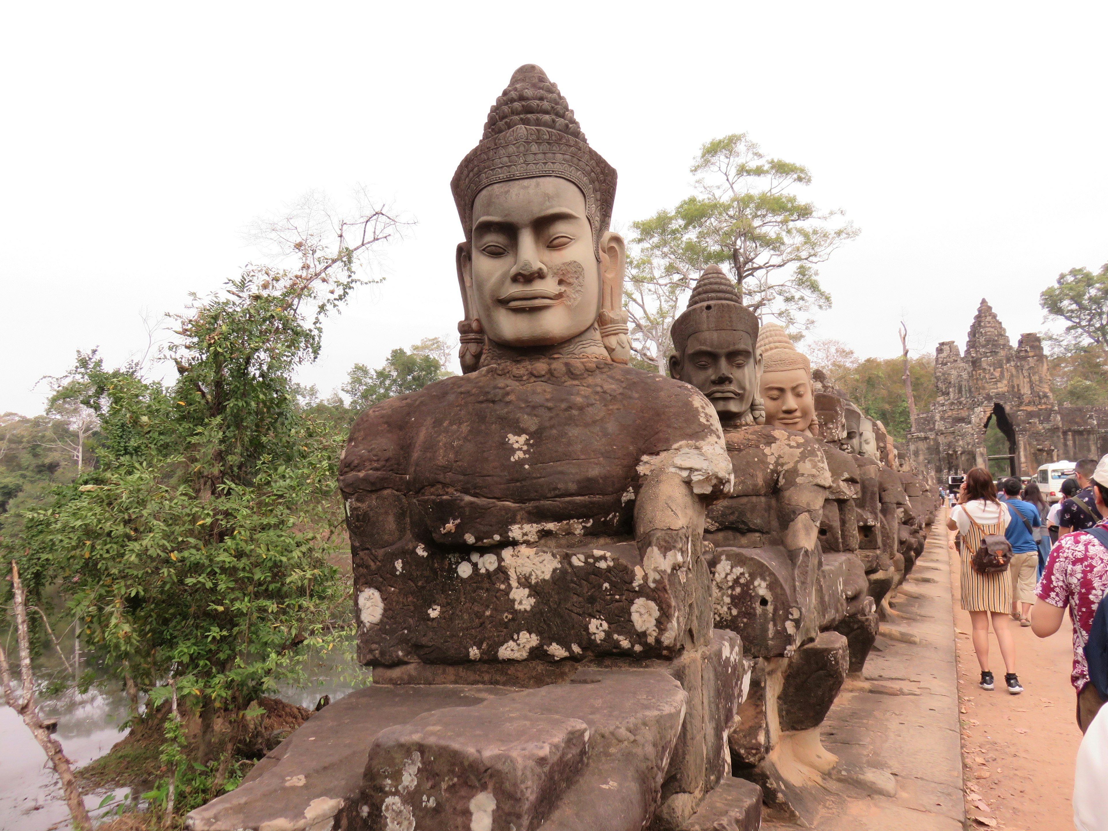 Stone sculptures lining a pathway near Angkor Wat surrounded by lush greenery