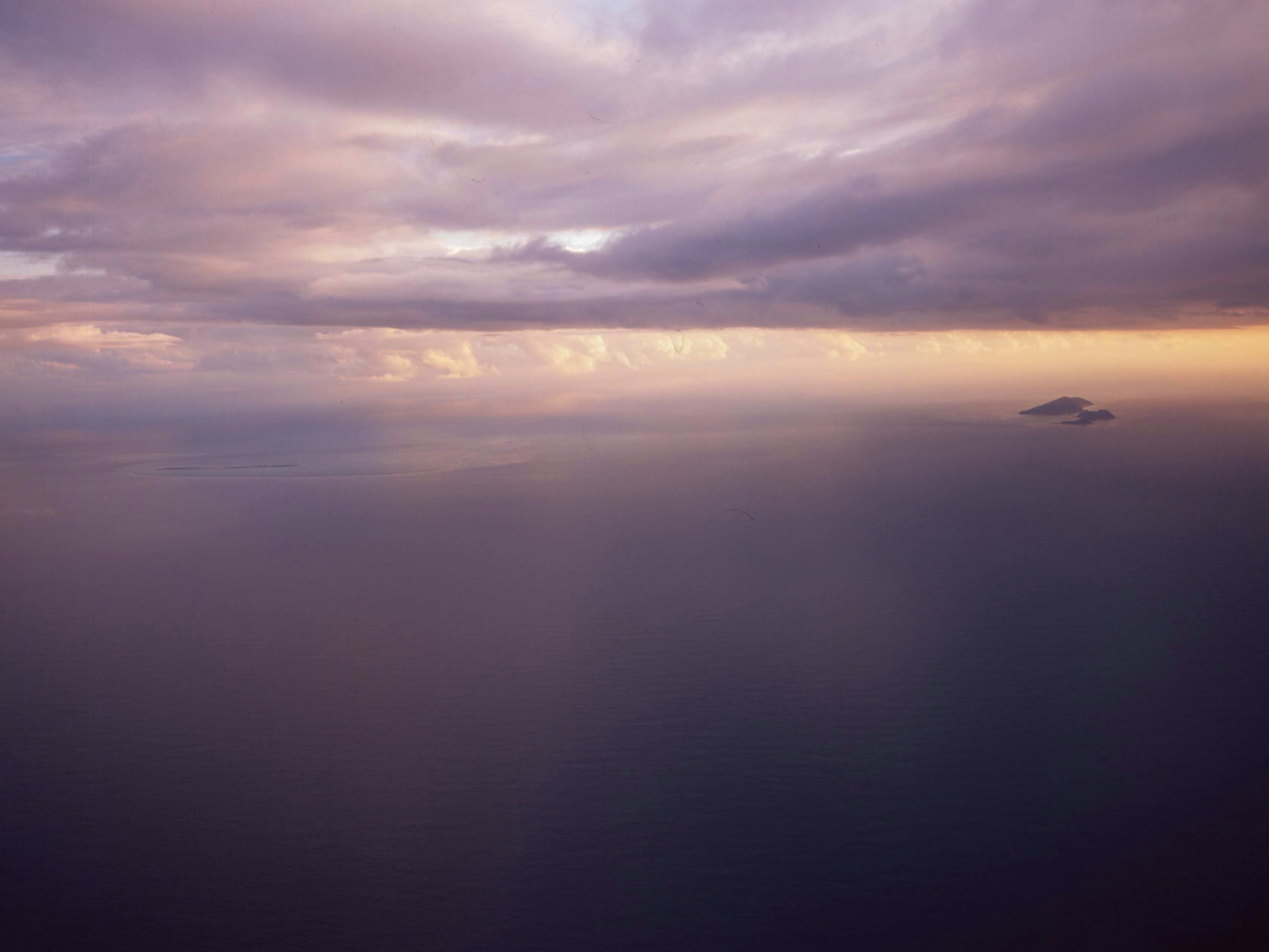 空の紫色の雲と海の景色に小さな島が見える