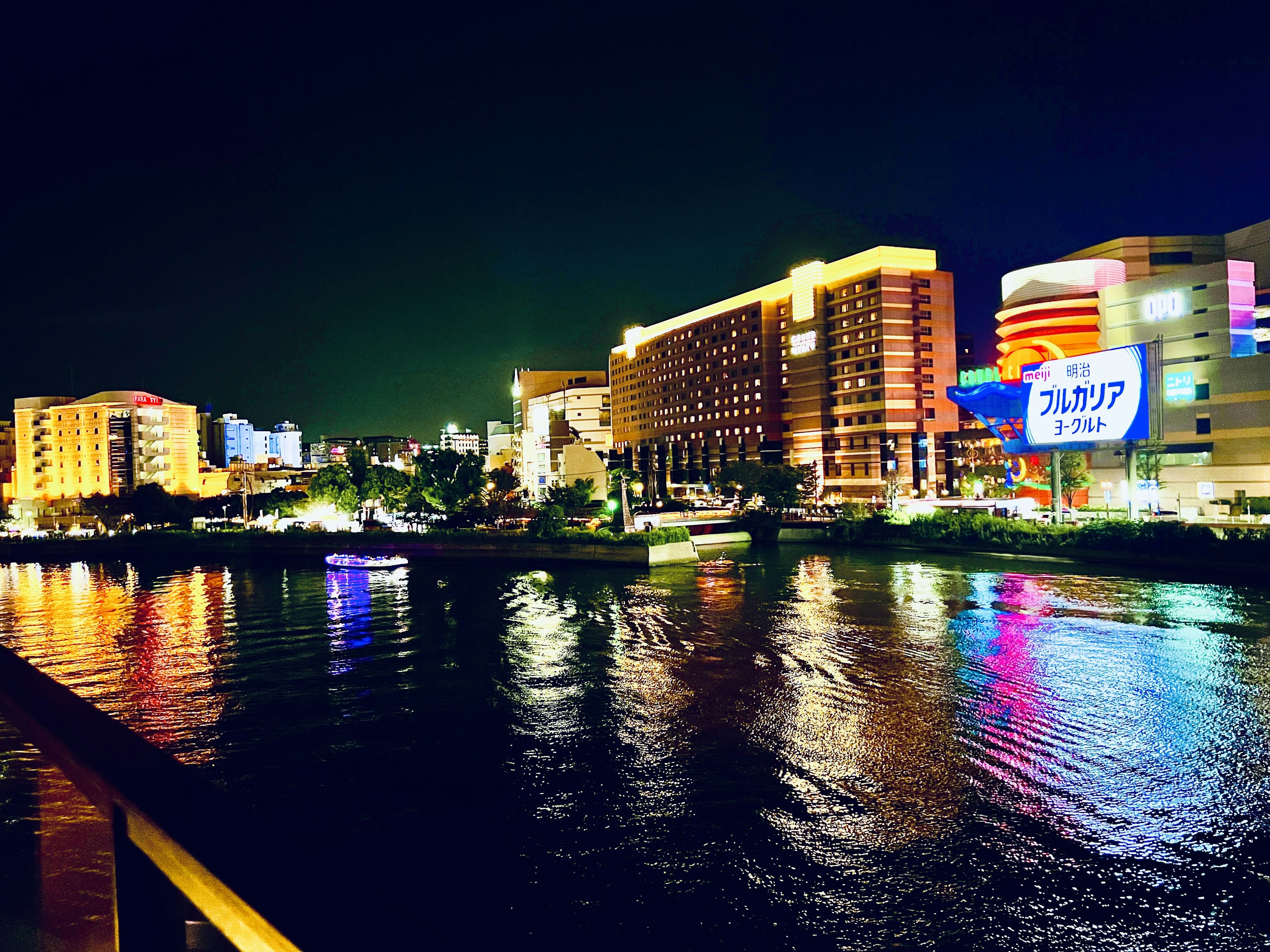 Paisaje urbano nocturno a lo largo de un río con edificios iluminados y reflejos coloridos