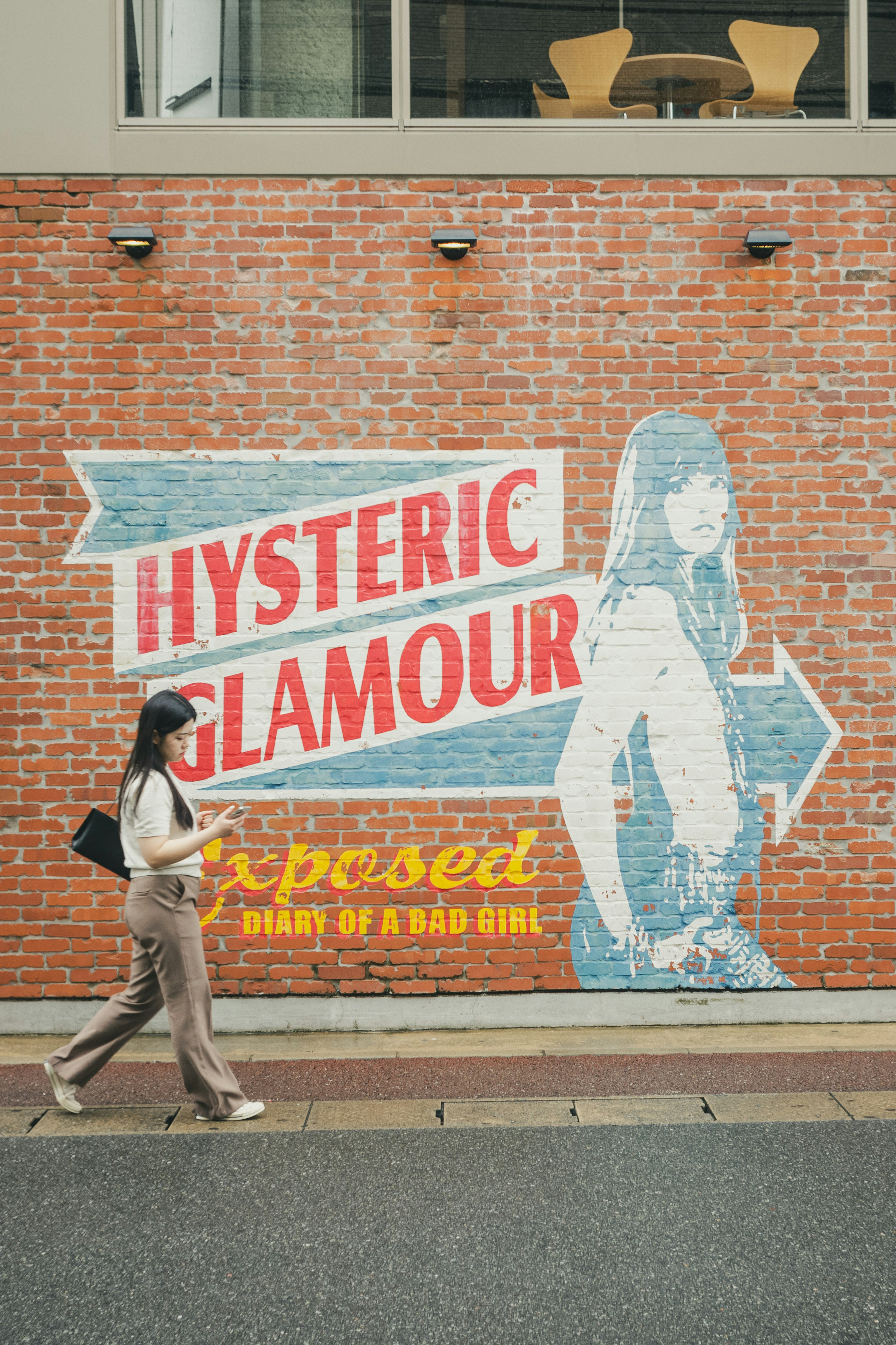 赤レンガの壁に描かれた「HYSTERIC GLAMOUR」のグラフィックアートを背景にした女性