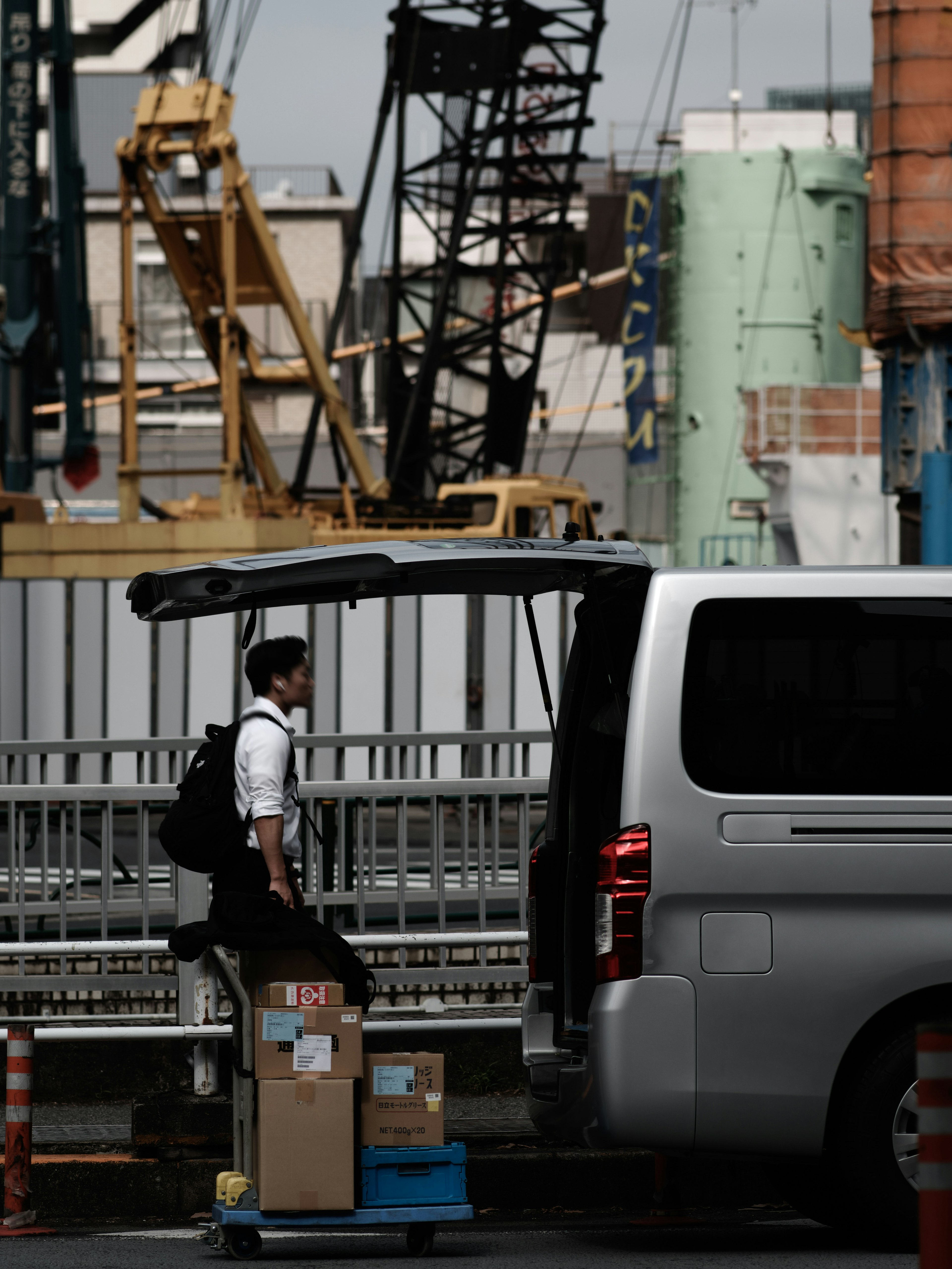 Man loading boxes into a van with cranes in the background at a port