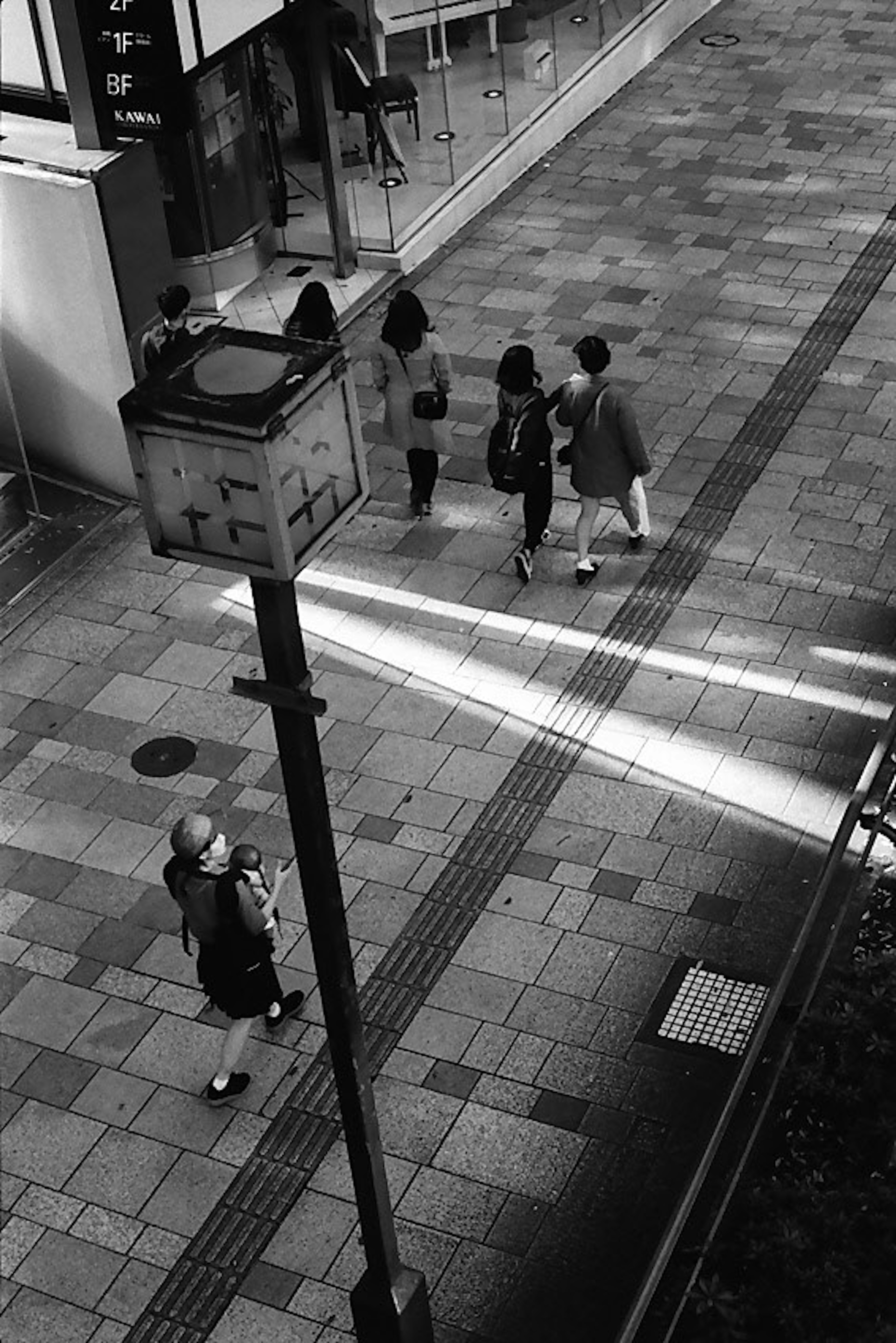 Escena urbana en blanco y negro con personas caminando y una farola