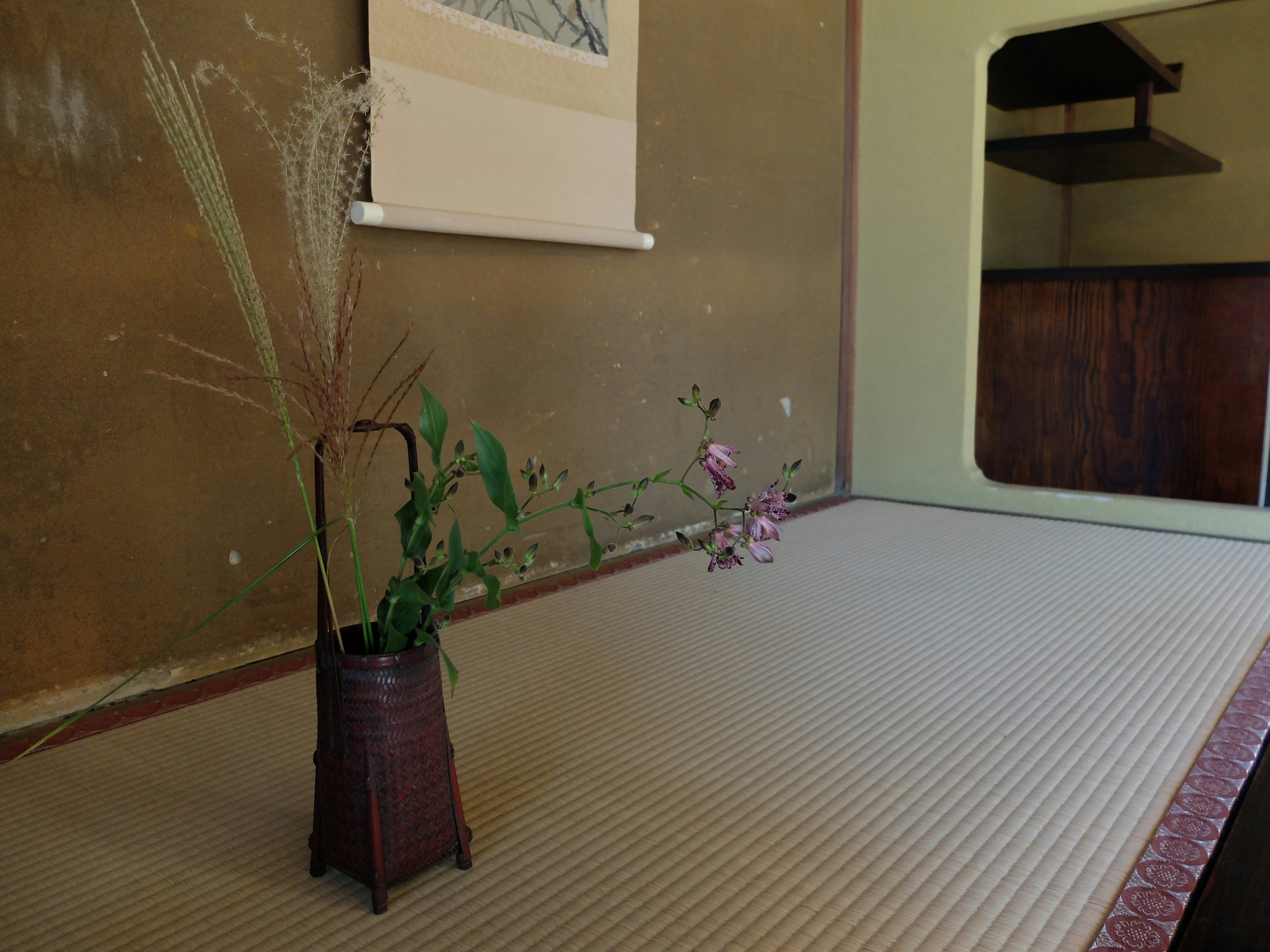 A simple Japanese room with tatami flooring featuring a vase and floral arrangement