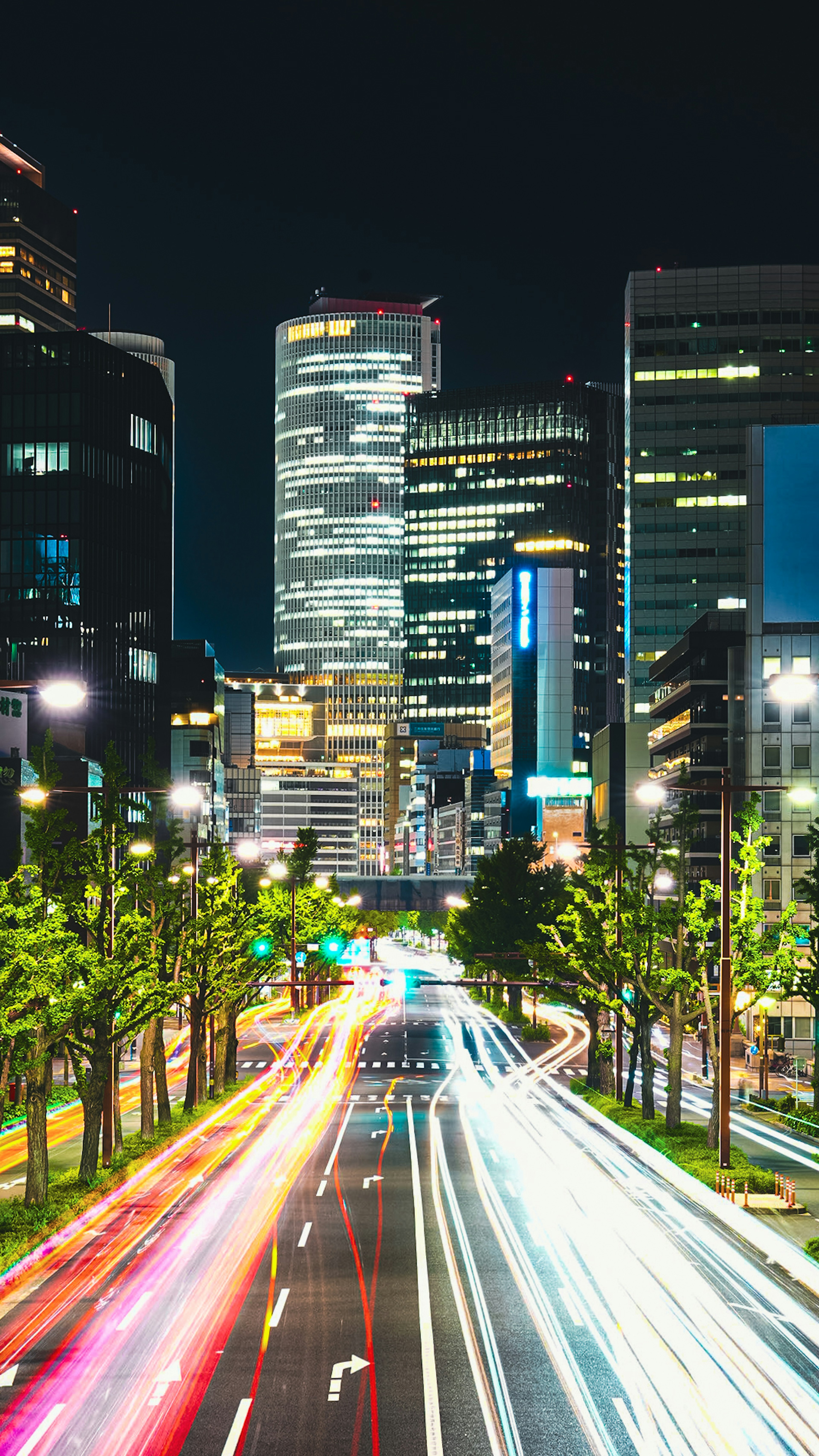 Paesaggio urbano notturno con edifici luminosi e luci di auto in movimento