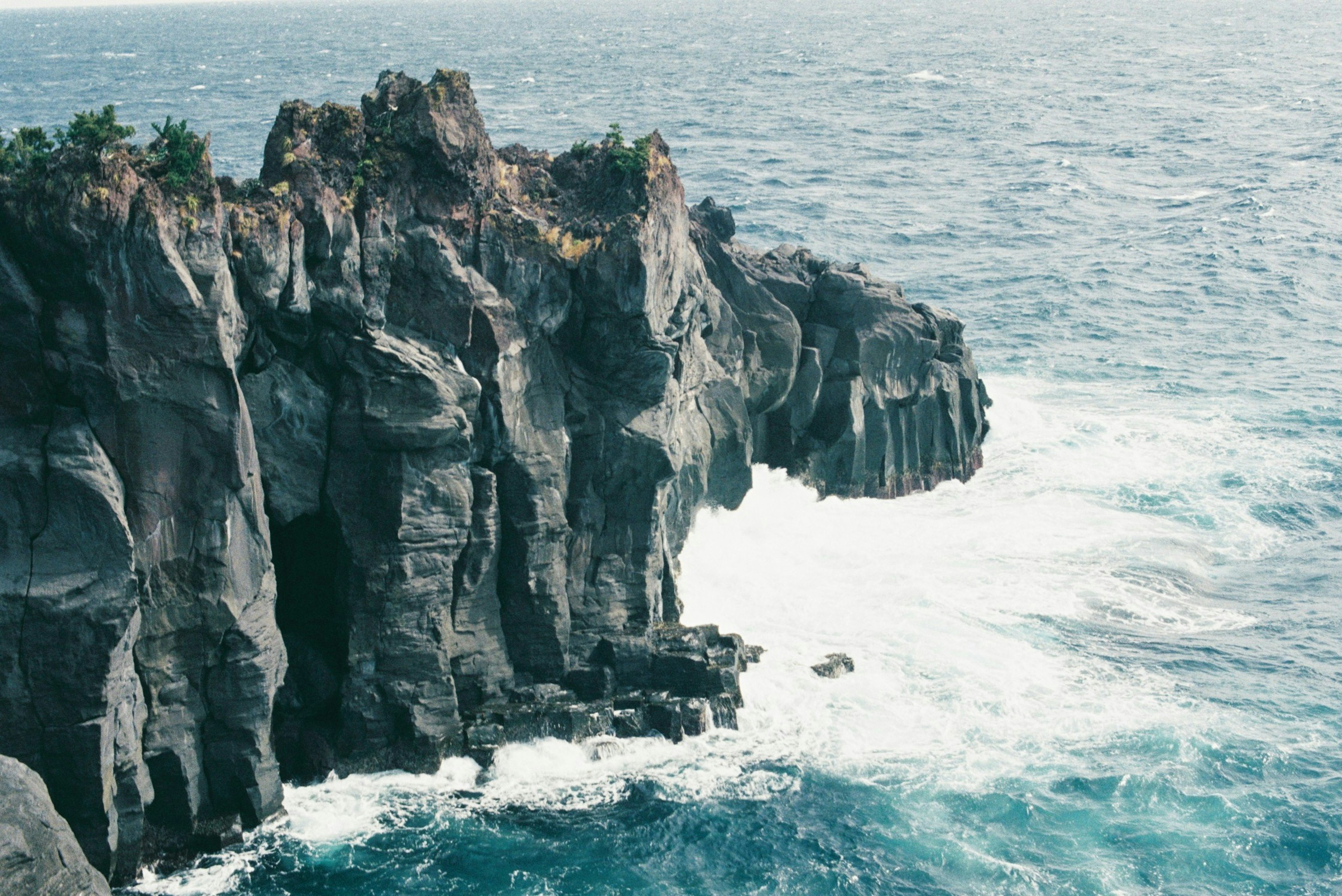 Scogliera rocciosa che si affaccia sull'oceano con onde che si infrangono