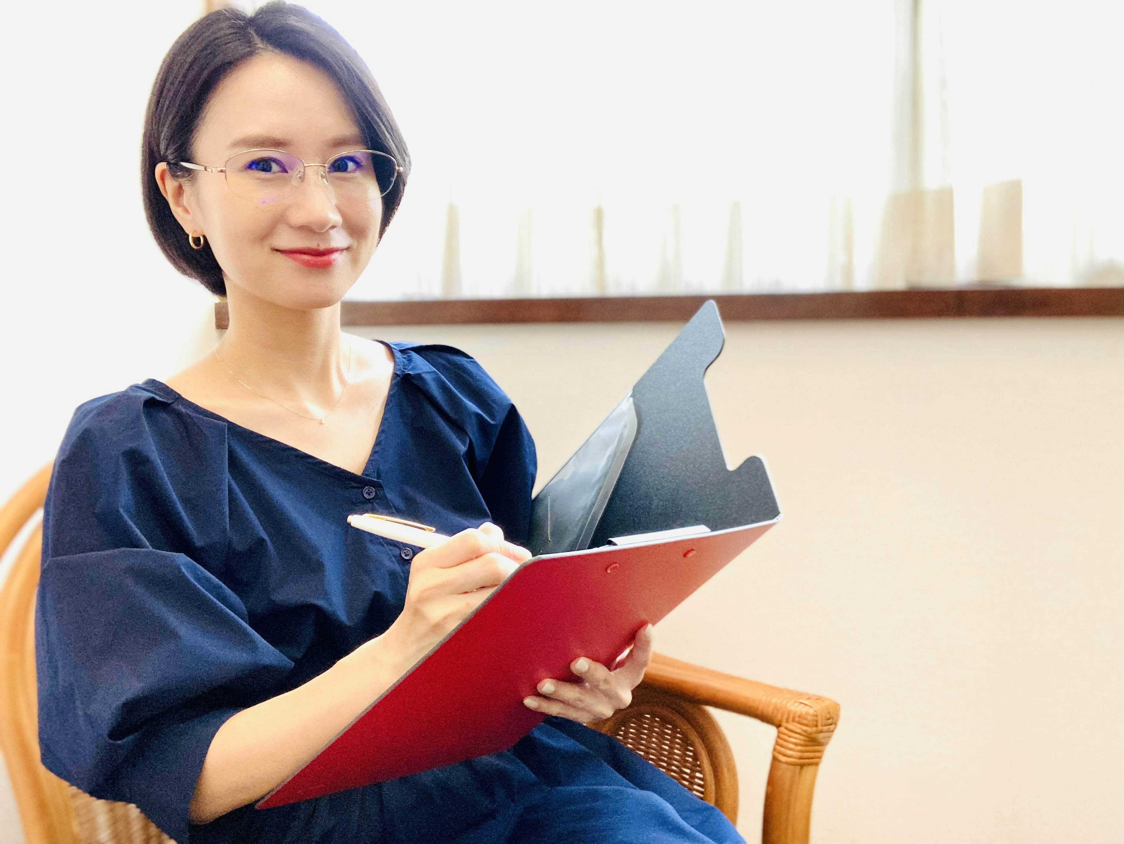 Una mujer con un atuendo azul sosteniendo una carpeta roja sonriendo