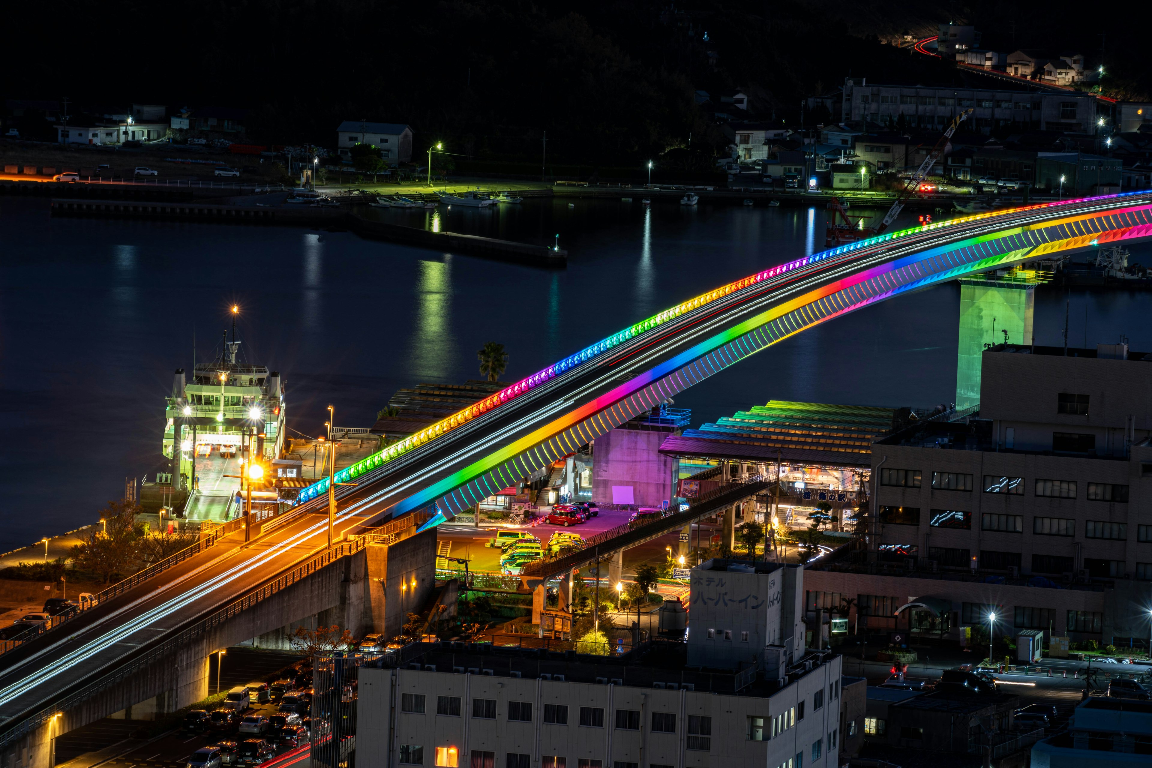 Vibrant rainbow bridge illuminated at night over a harbor