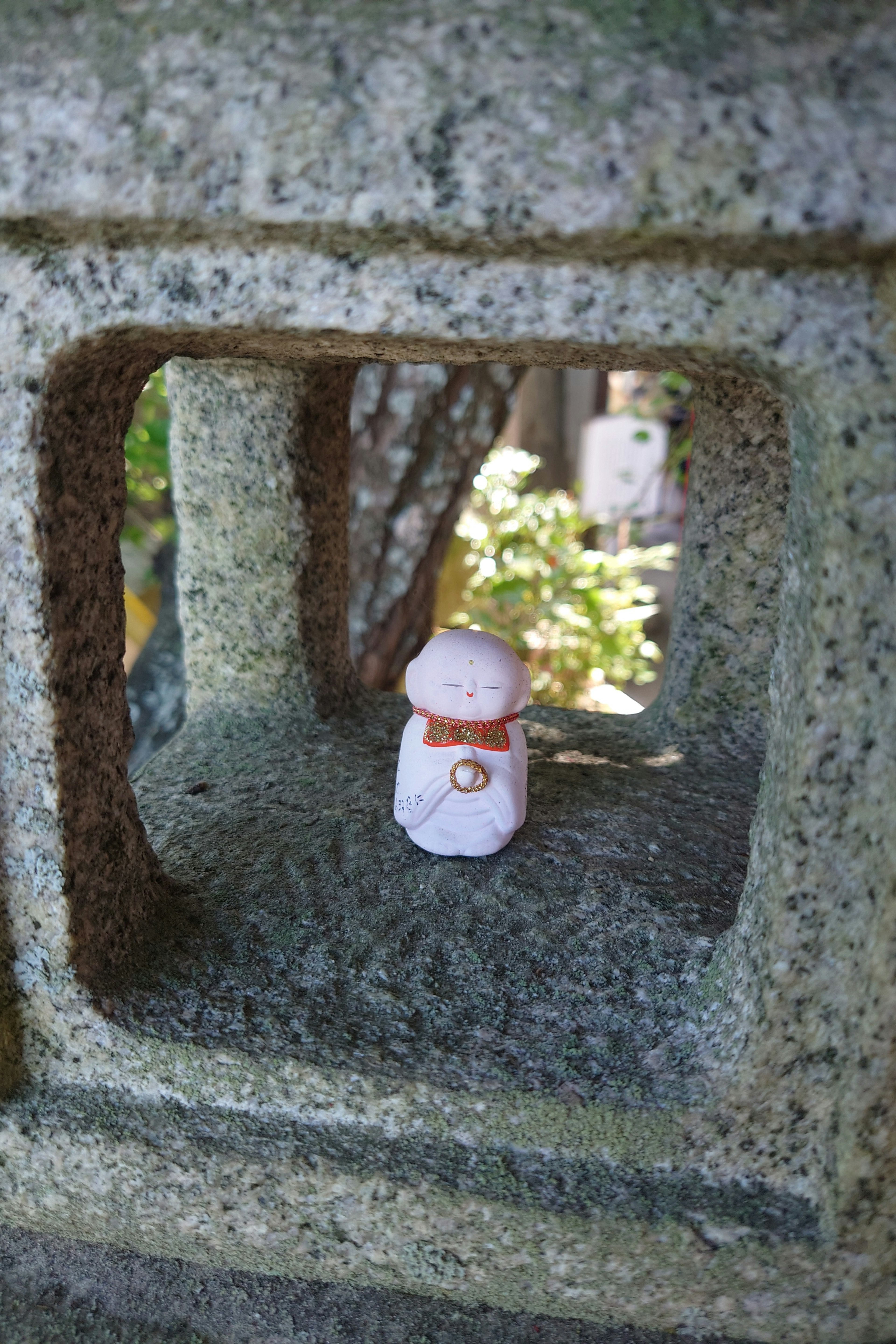 Small white figure visible through a stone lantern opening surrounded by greenery