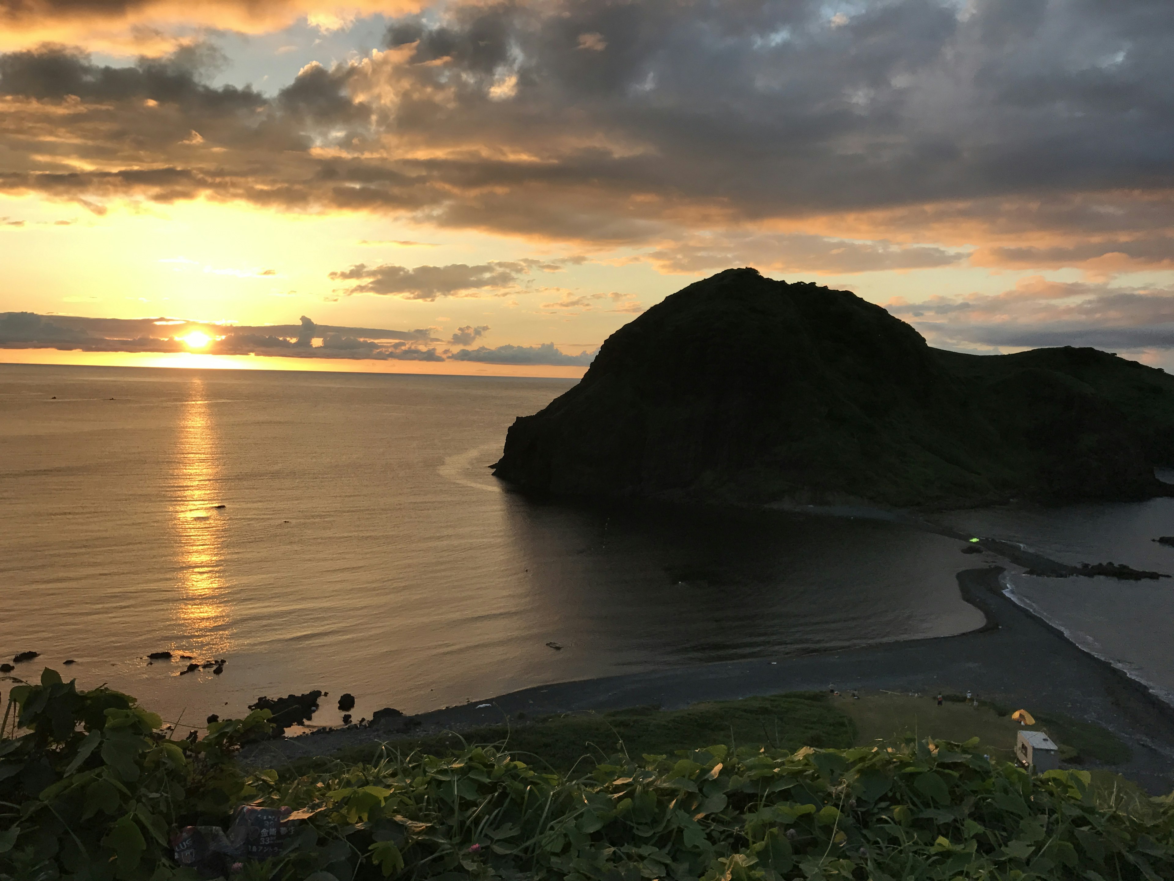 夕日が海に沈む美しい風景 緑の草と黒い山が特徴的