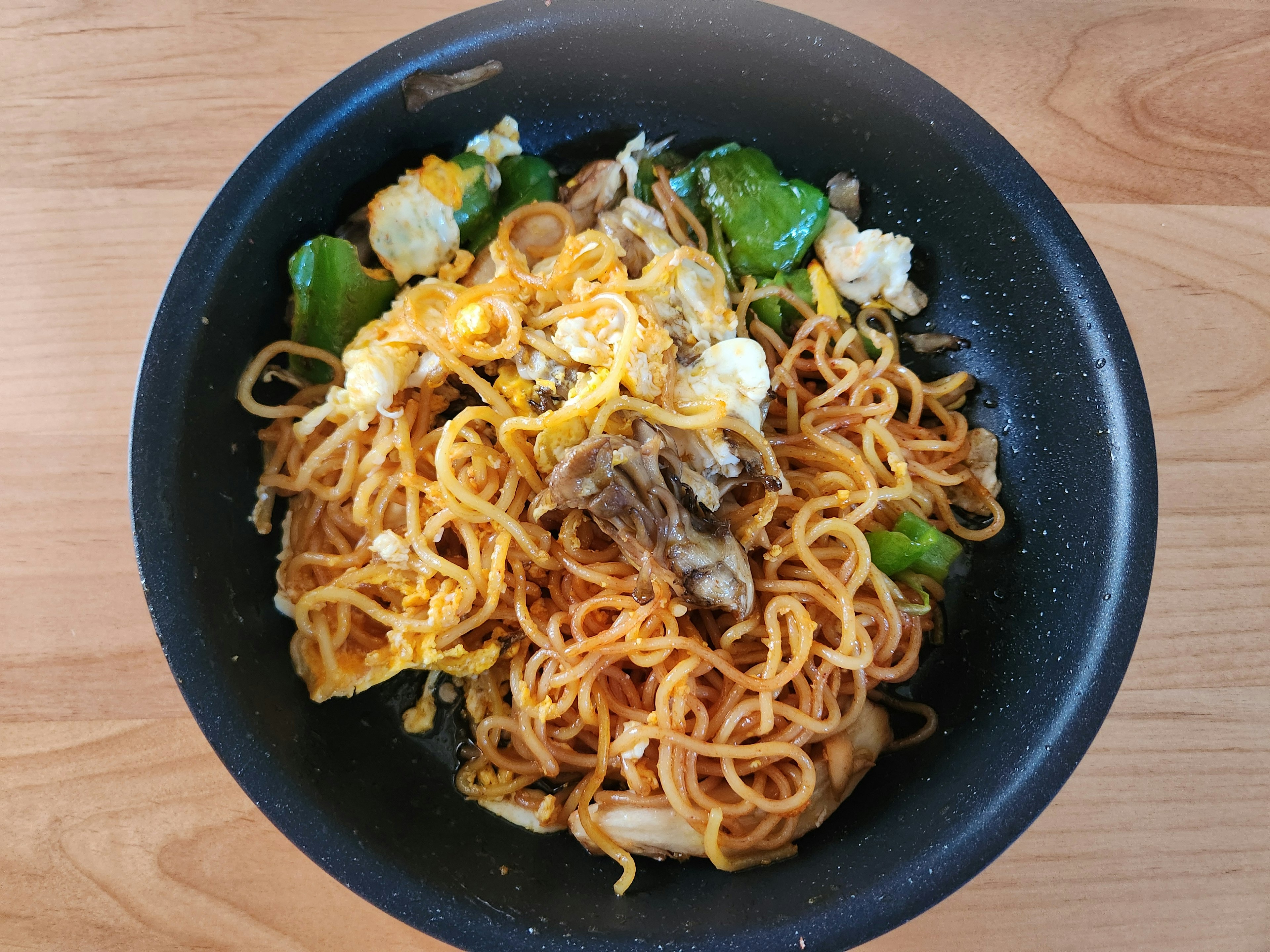 黒いボウルに盛られた焼きそばと野菜の料理