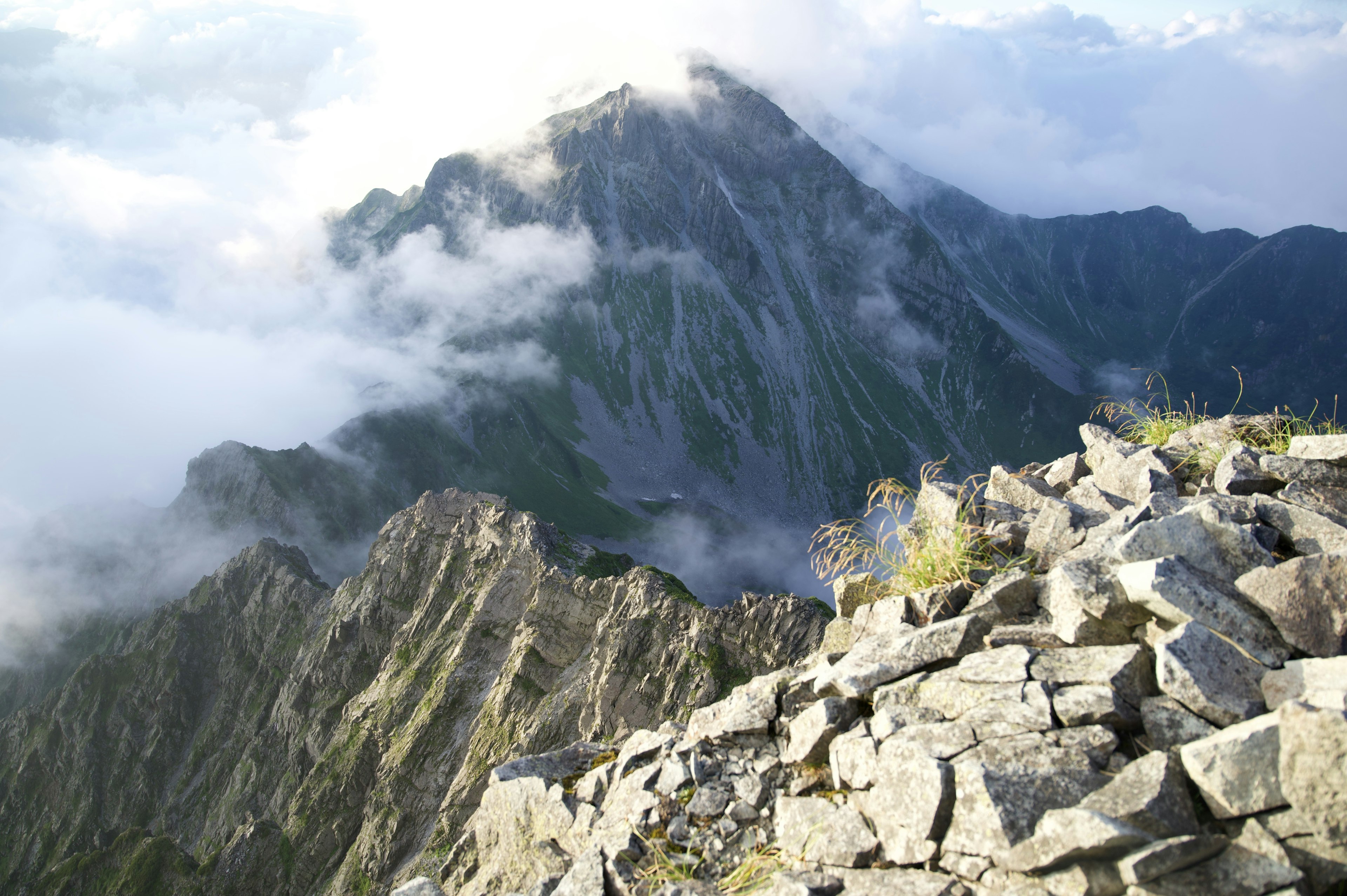 Pemandangan gunung dengan awan dan latar depan berbatu