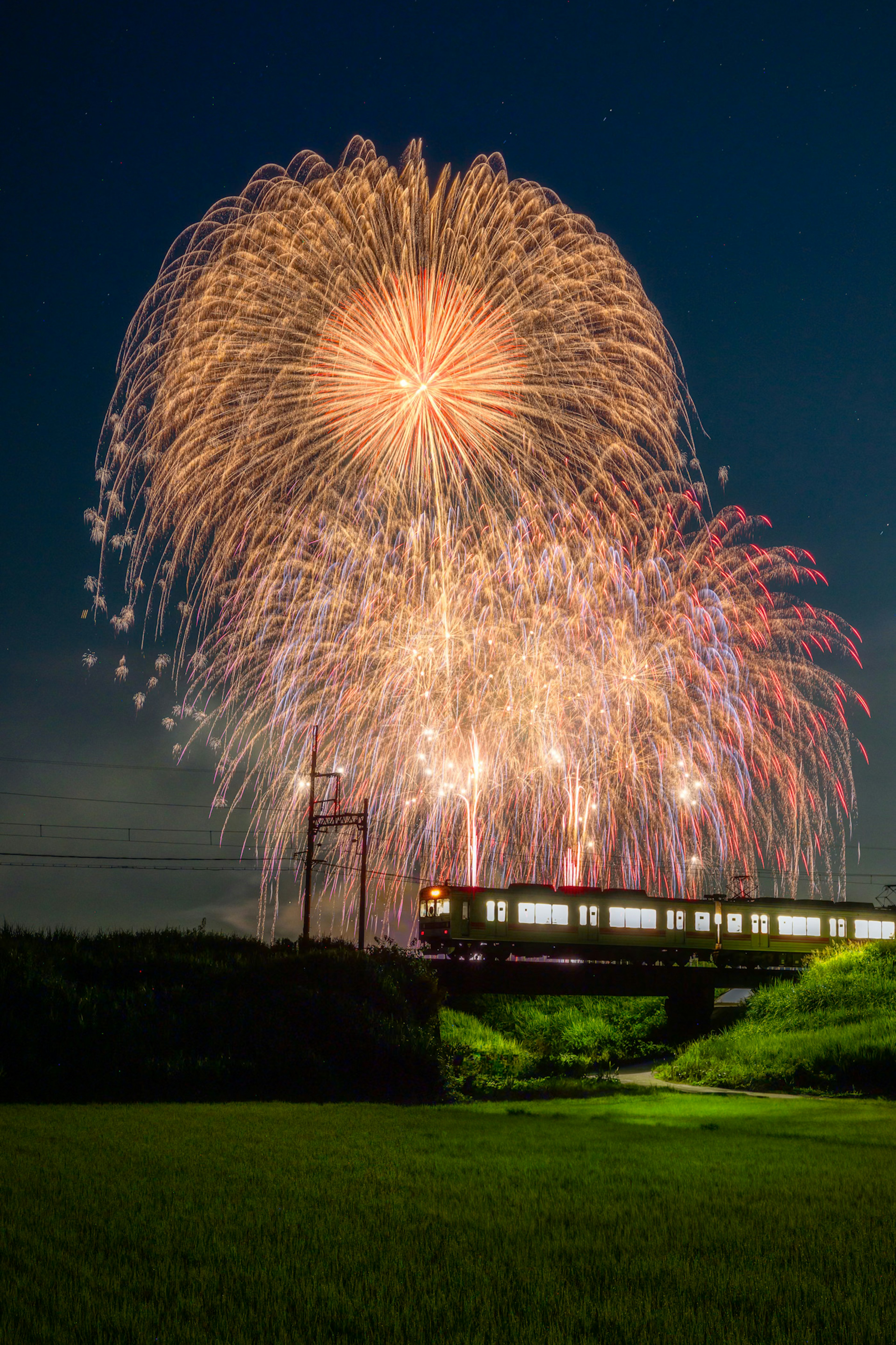 夜空に花火が打ち上がる中を走る列車の風景