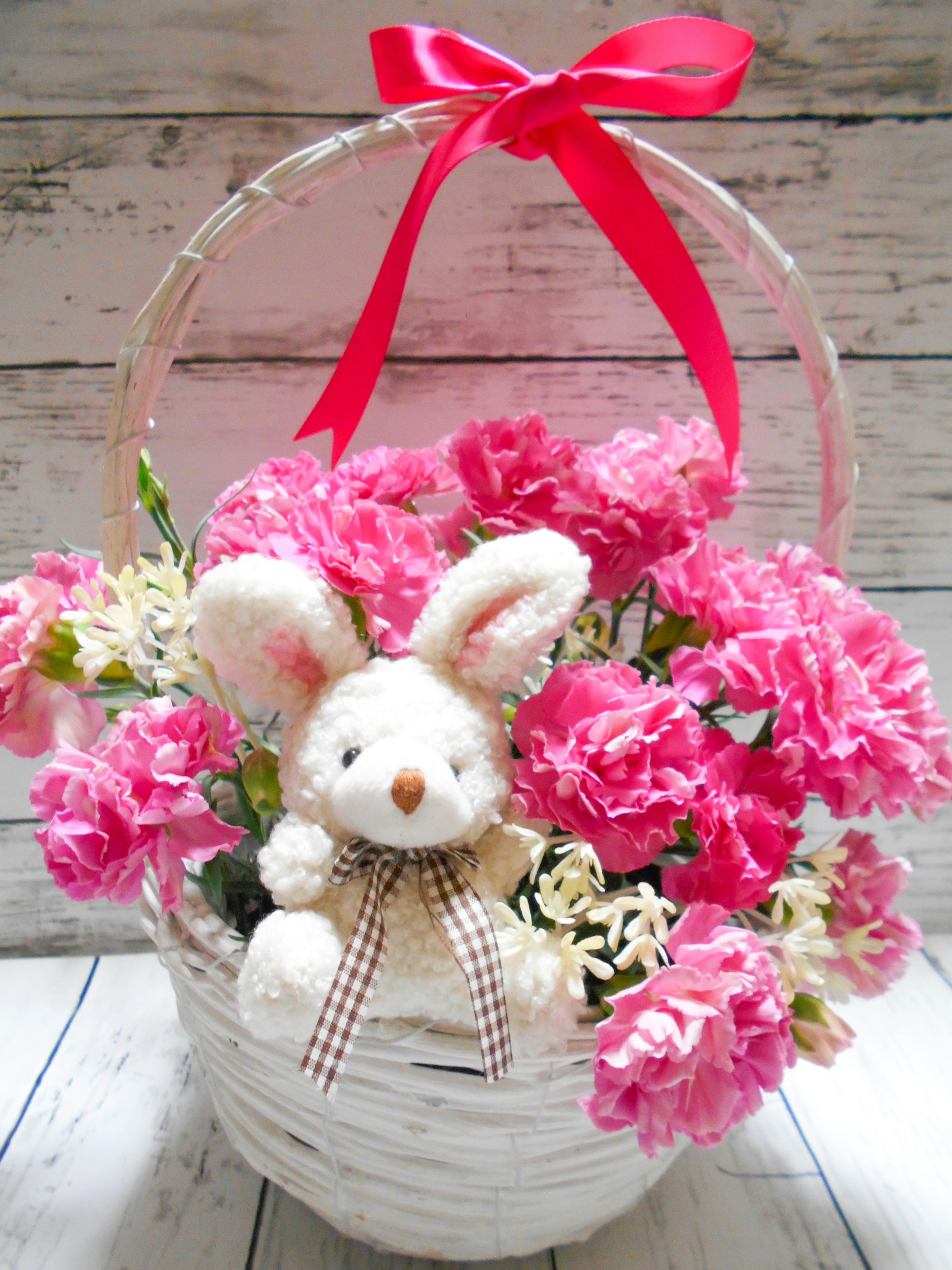 A basket filled with pink flowers and a bunny plush toy