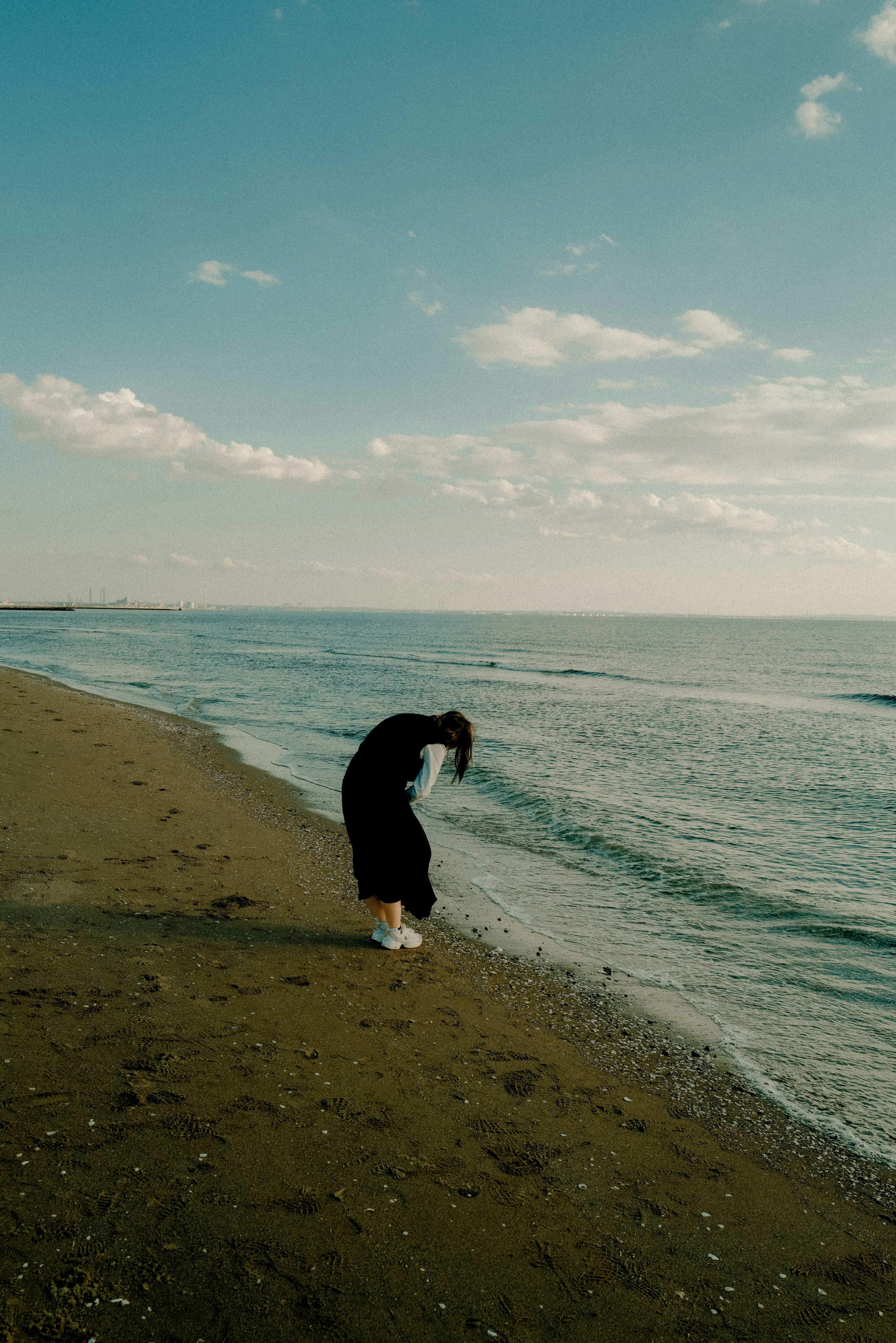 Silhouette di una donna che scuote i capelli sulla spiaggia con cielo blu e onde