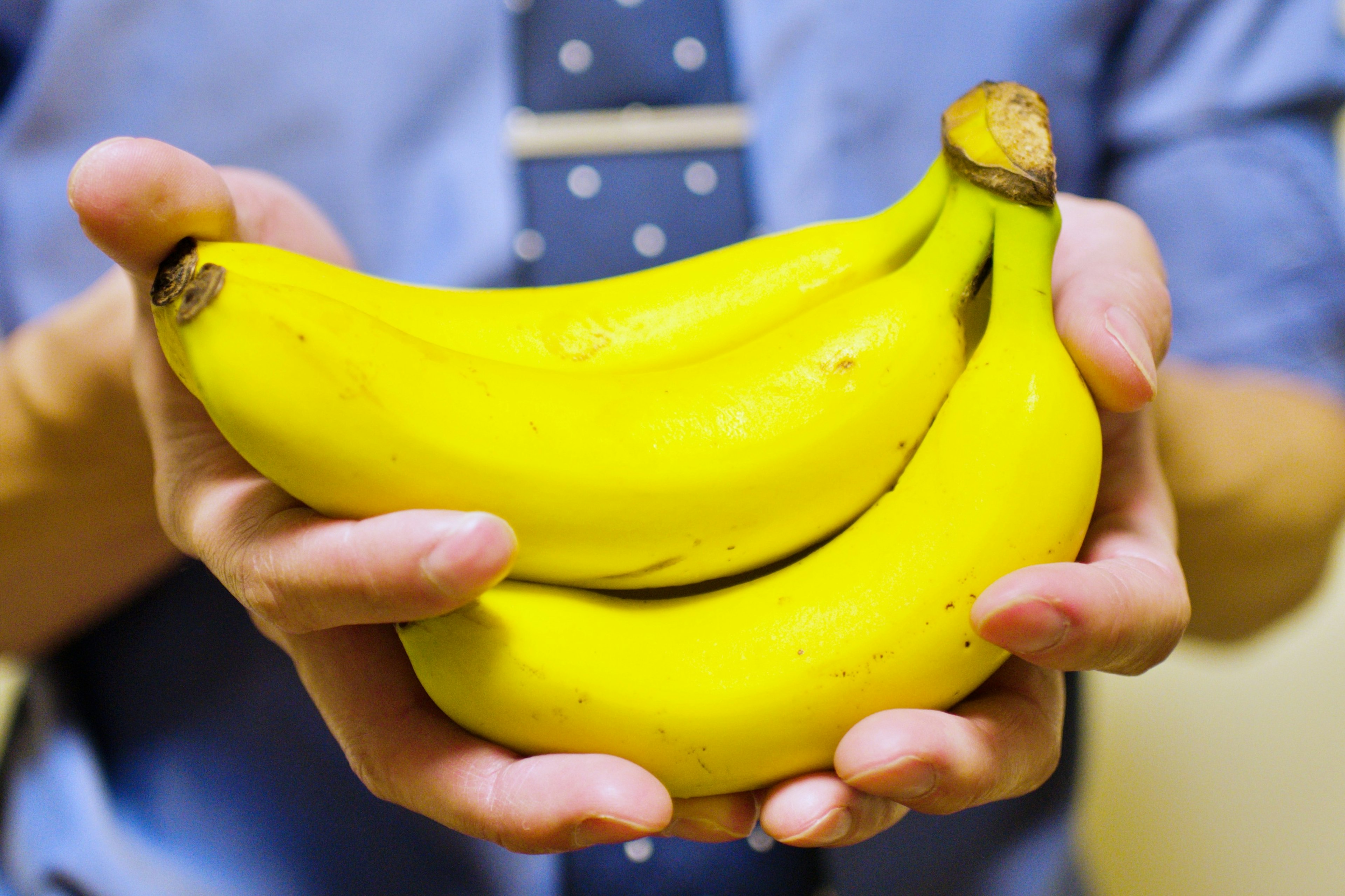 Un homme en chemise bleue et cravate tenant des bananes