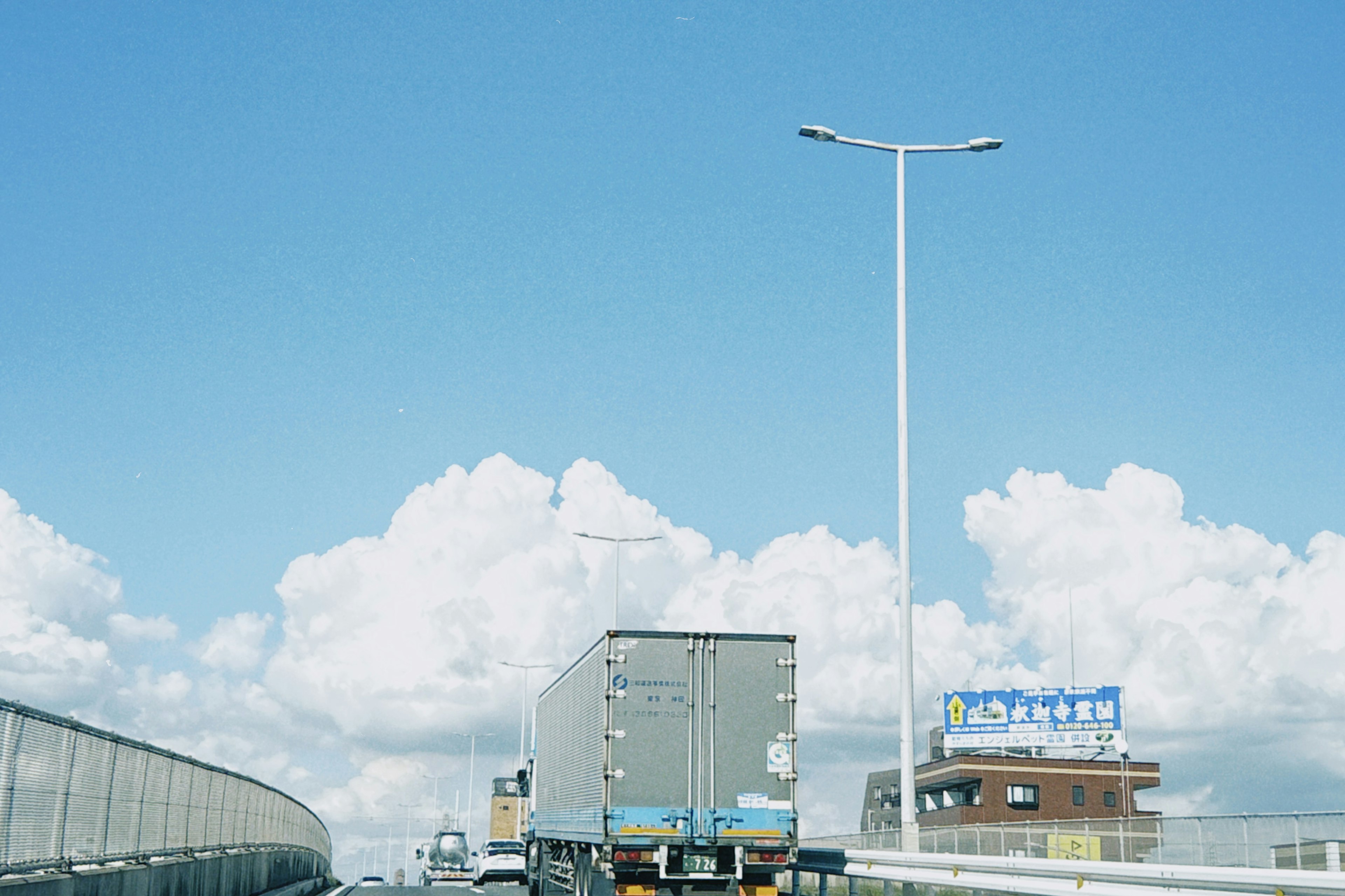 Truk melaju di jalan tol di bawah langit biru dengan awan berbulu