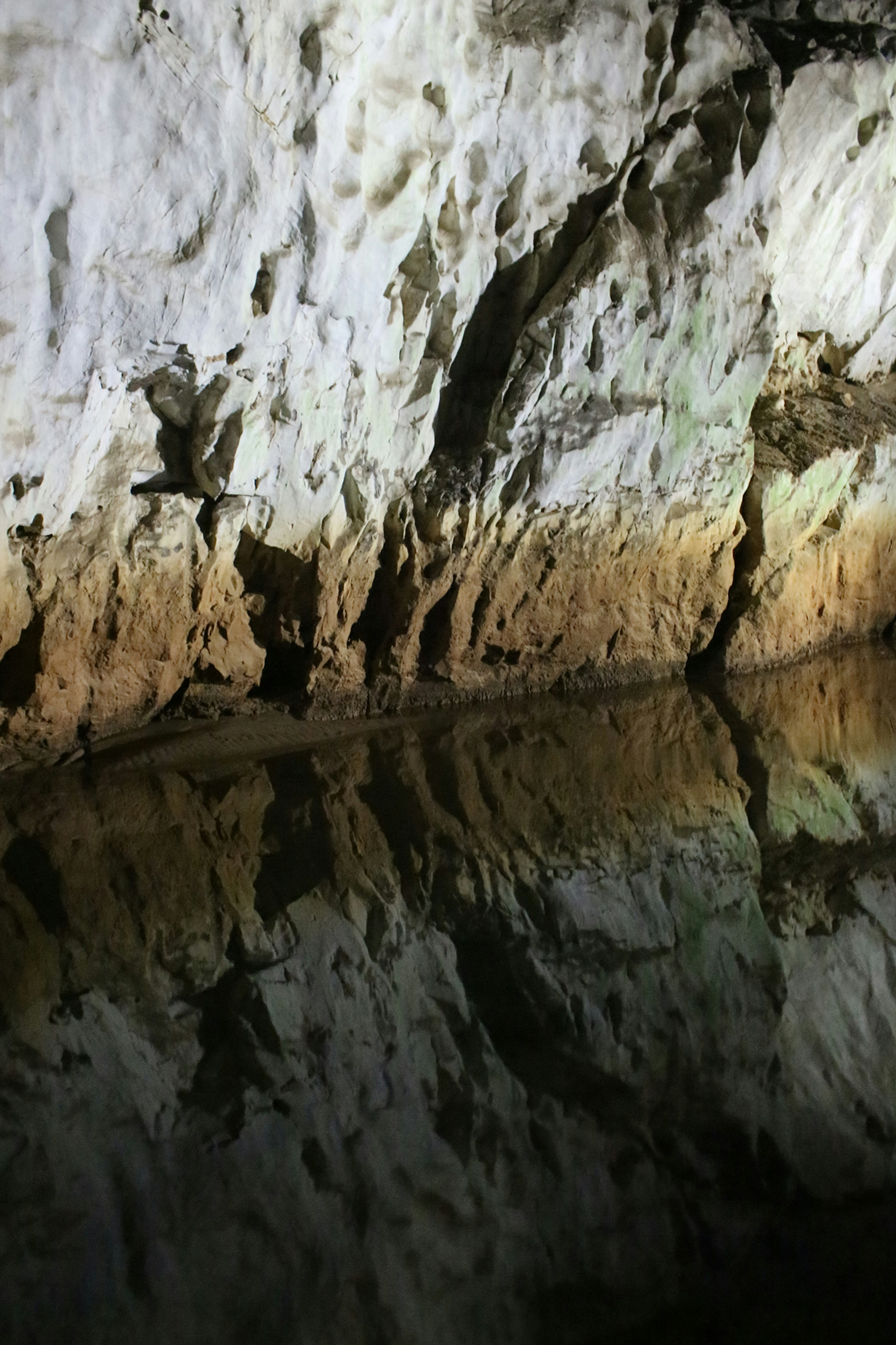 Dinding gua dengan batu putih dan refleksi di permukaan air